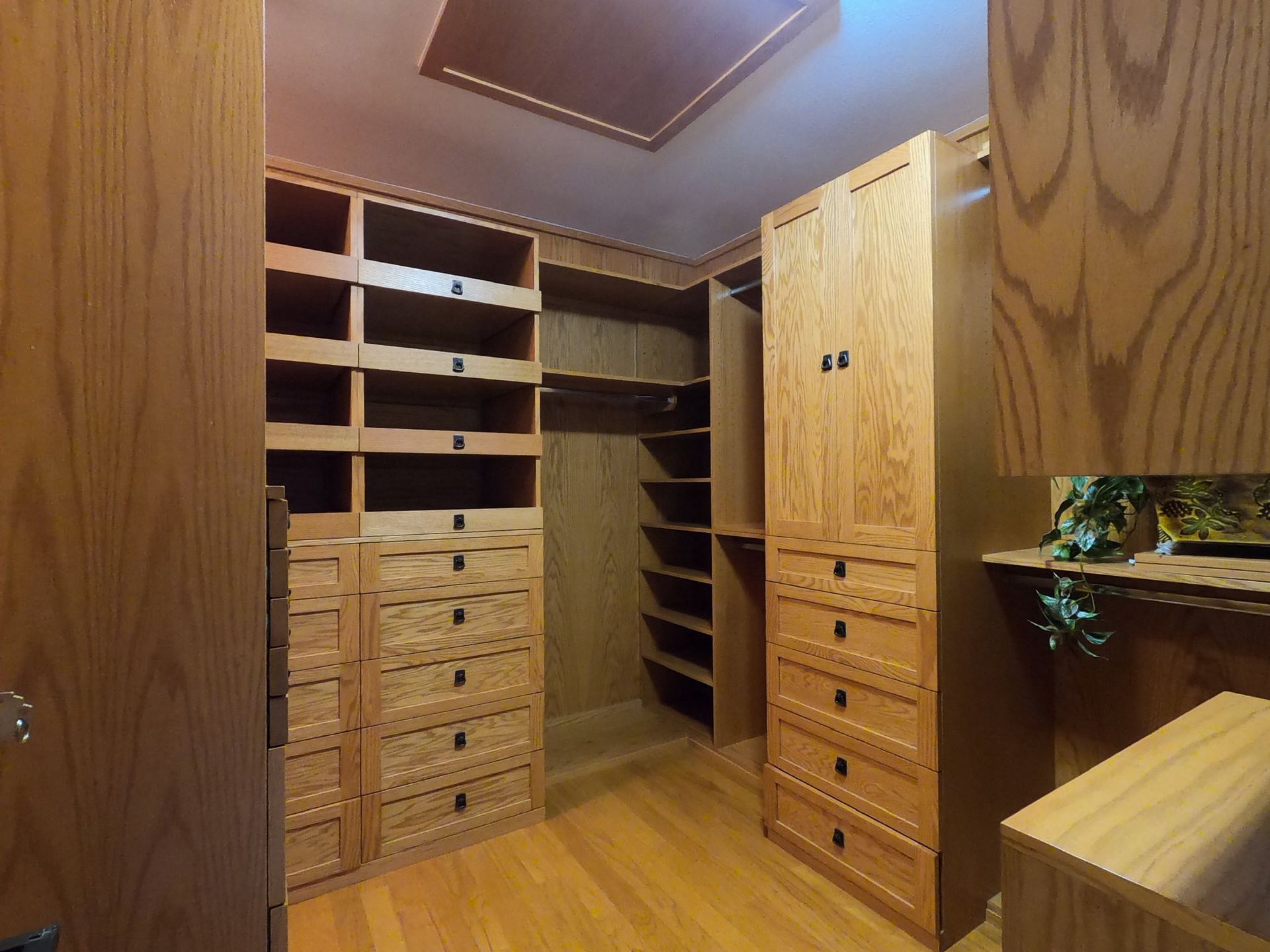Walk-in closet with custom oak shelving, drawers, and hanging space; light wood floors and ceiling.