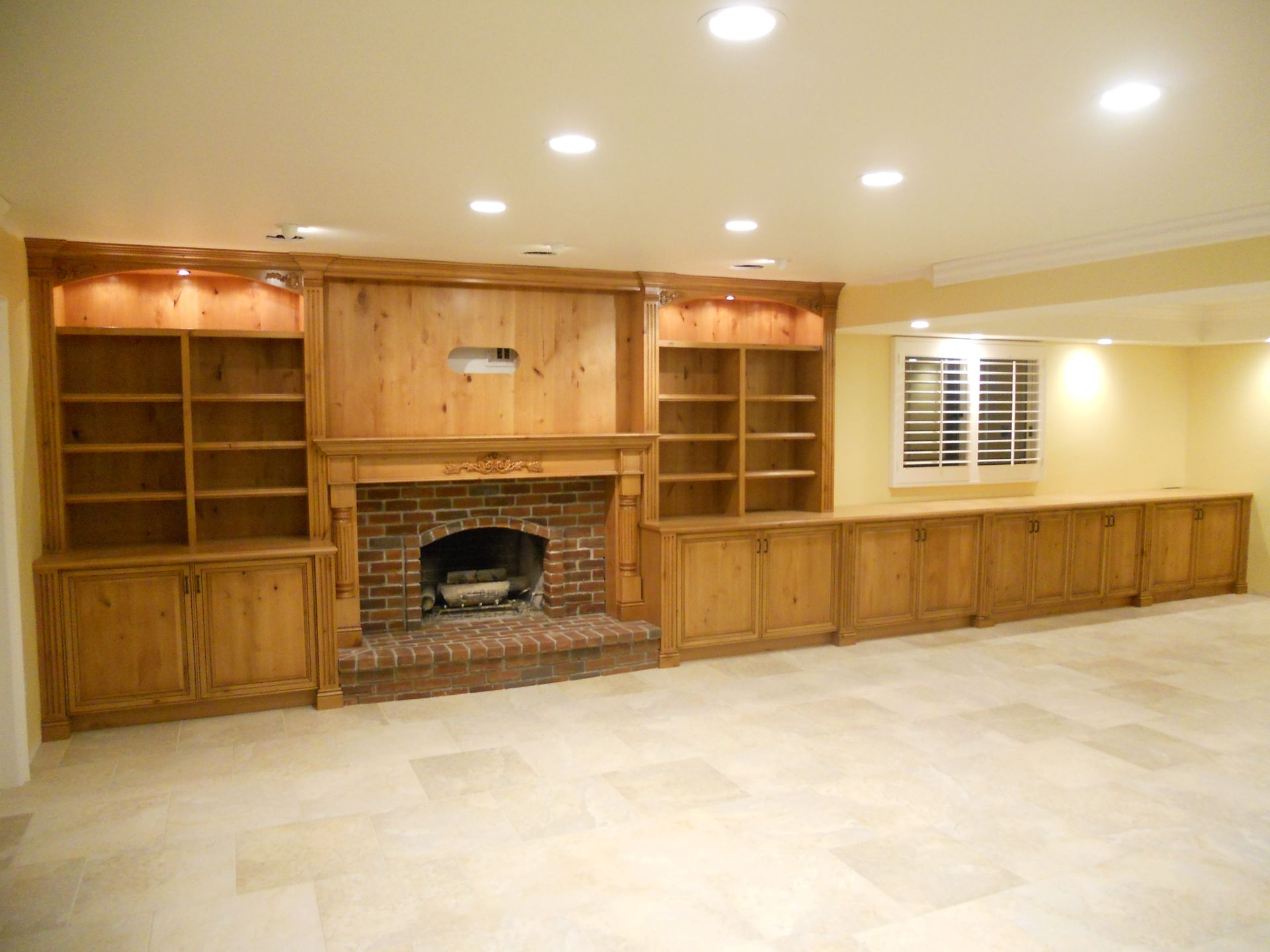 Fireplace with built-in bookshelves and cabinets, beige flooring, lit by recessed ceiling lights, in an empty room.