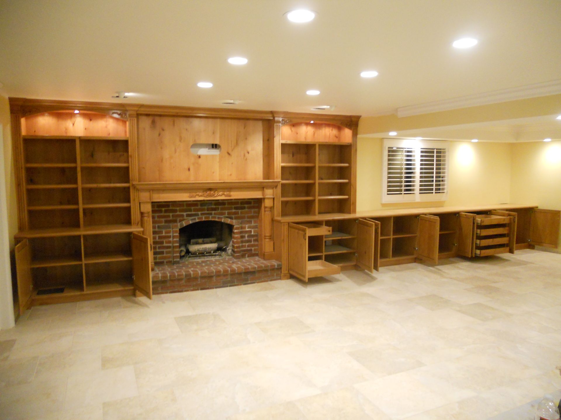 Built-in wooden bookshelves, cabinets, and fireplace in a room with light-colored flooring and walls.