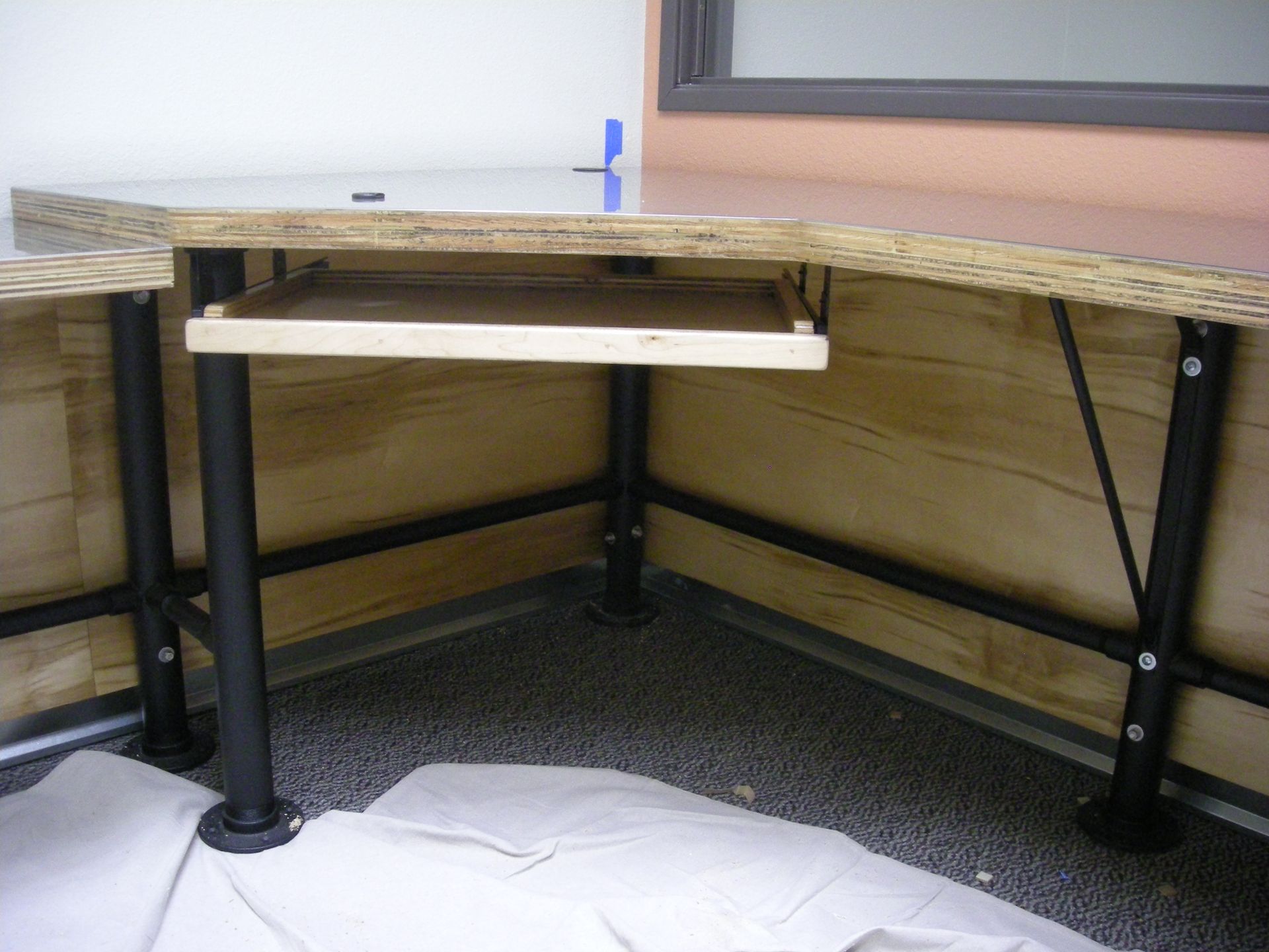 Corner desk with keyboard tray, supported by black metal legs and crossbeams.