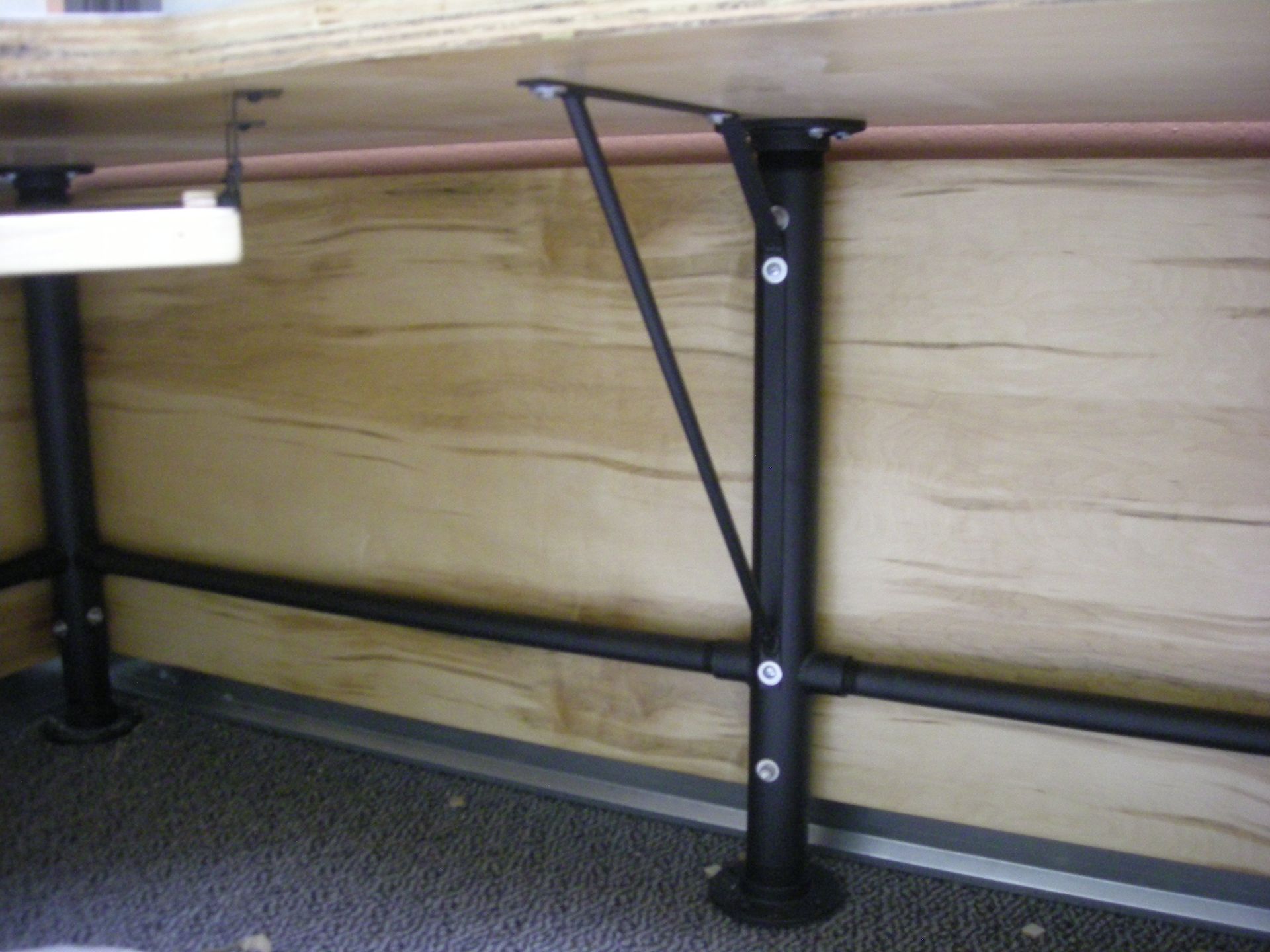 Black metal table supports bolted to a wood surface and floor, with a supporting angled beam.