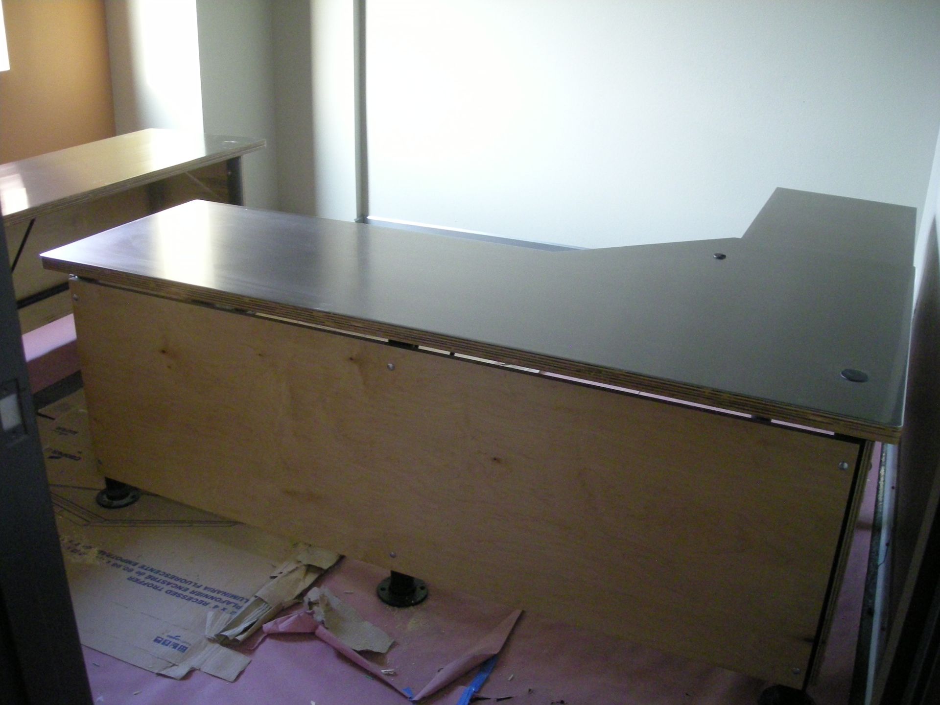 Large, light-wood office desk in room with another desk visible. Pink drop cloth and debris on floor.