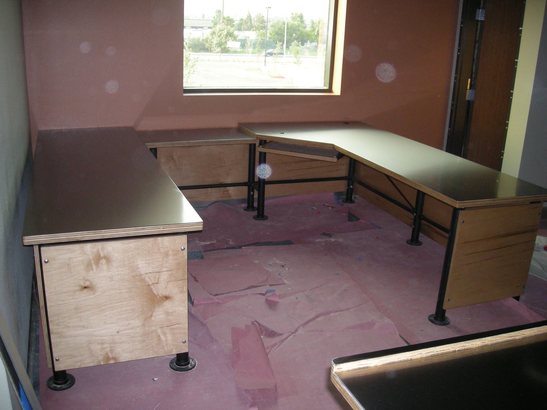 L-shaped desk in a room under construction, with a window and pink insulation on the floor.