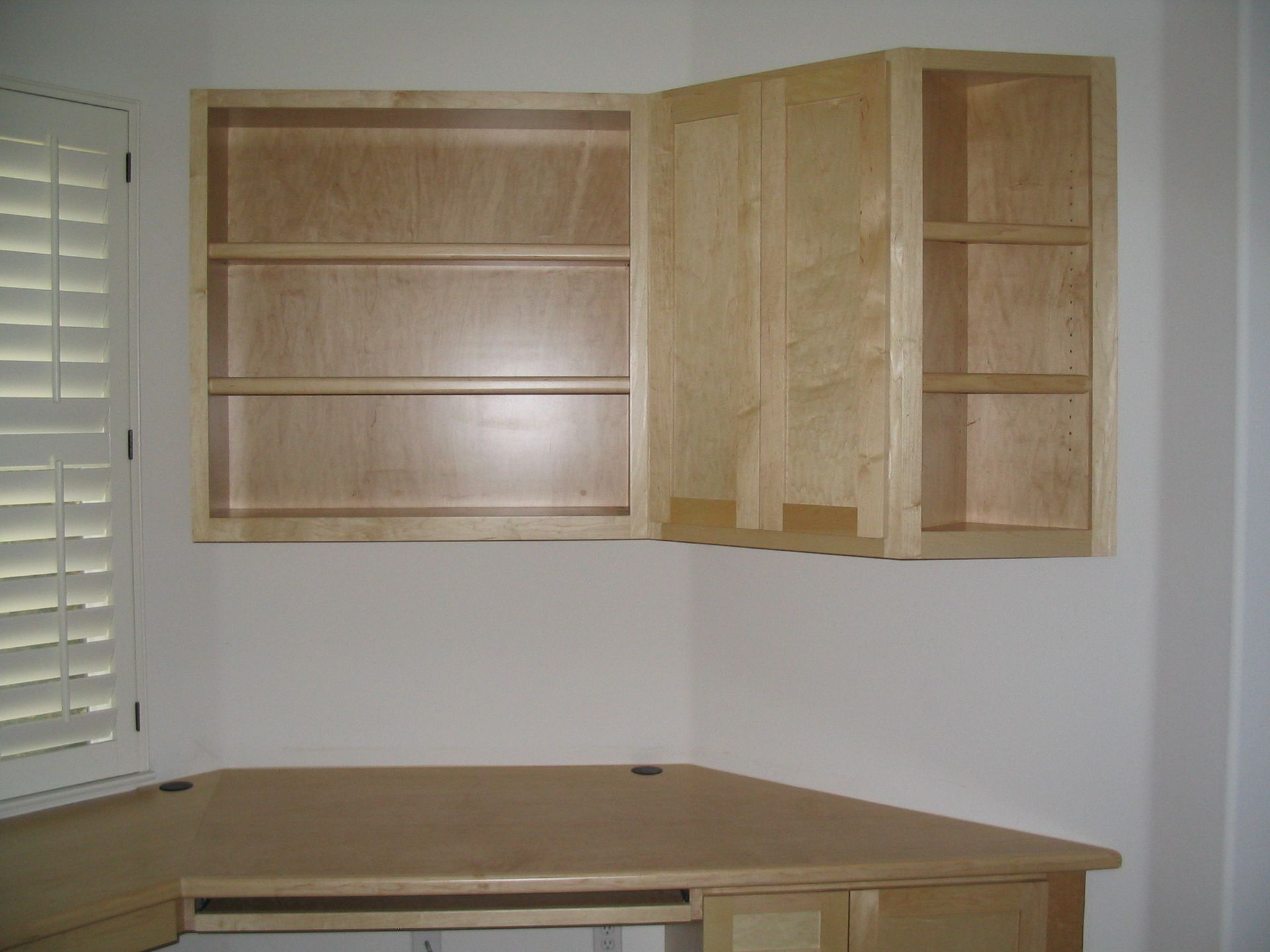 Corner desk with overhead cabinets; natural wood tones against a white wall.