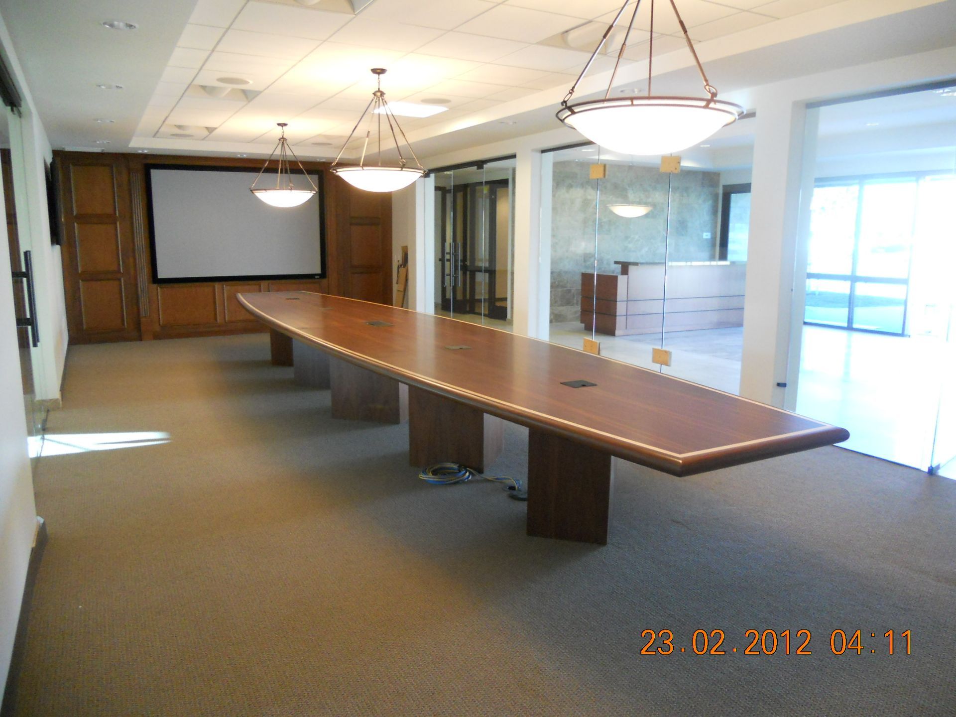 Conference room with long wooden table, screen, and three hanging lights.