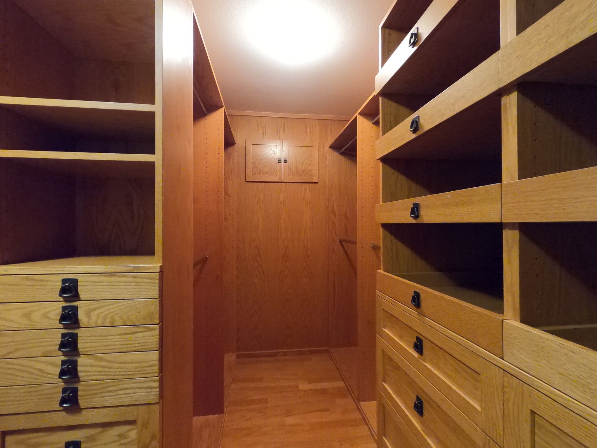 Walk-in closet with light wood shelving and drawers, a long narrow hallway, and a recessed ceiling light.