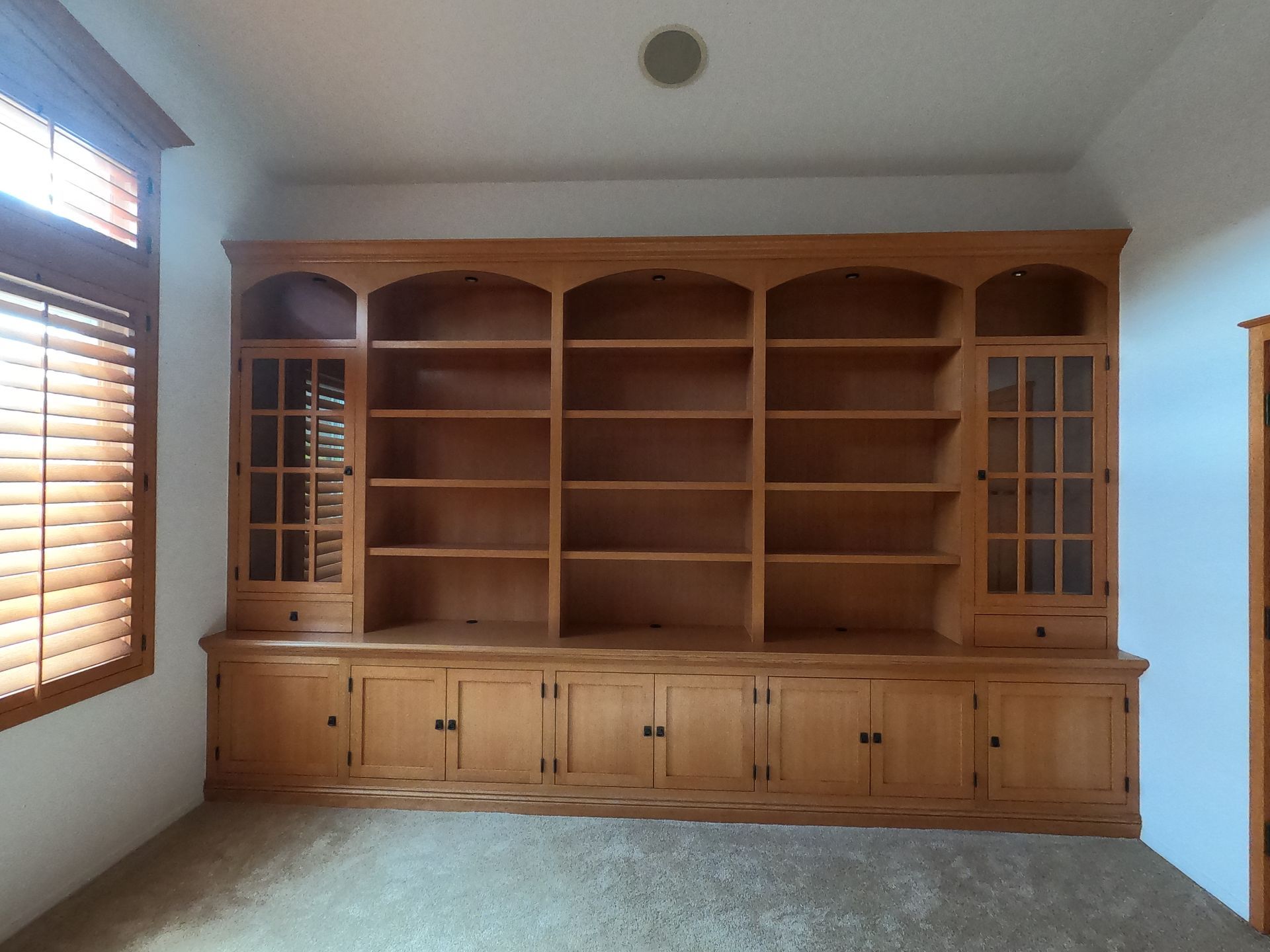 Built-in wooden bookshelf with upper shelves and lower cabinets in a room with a window and carpet.