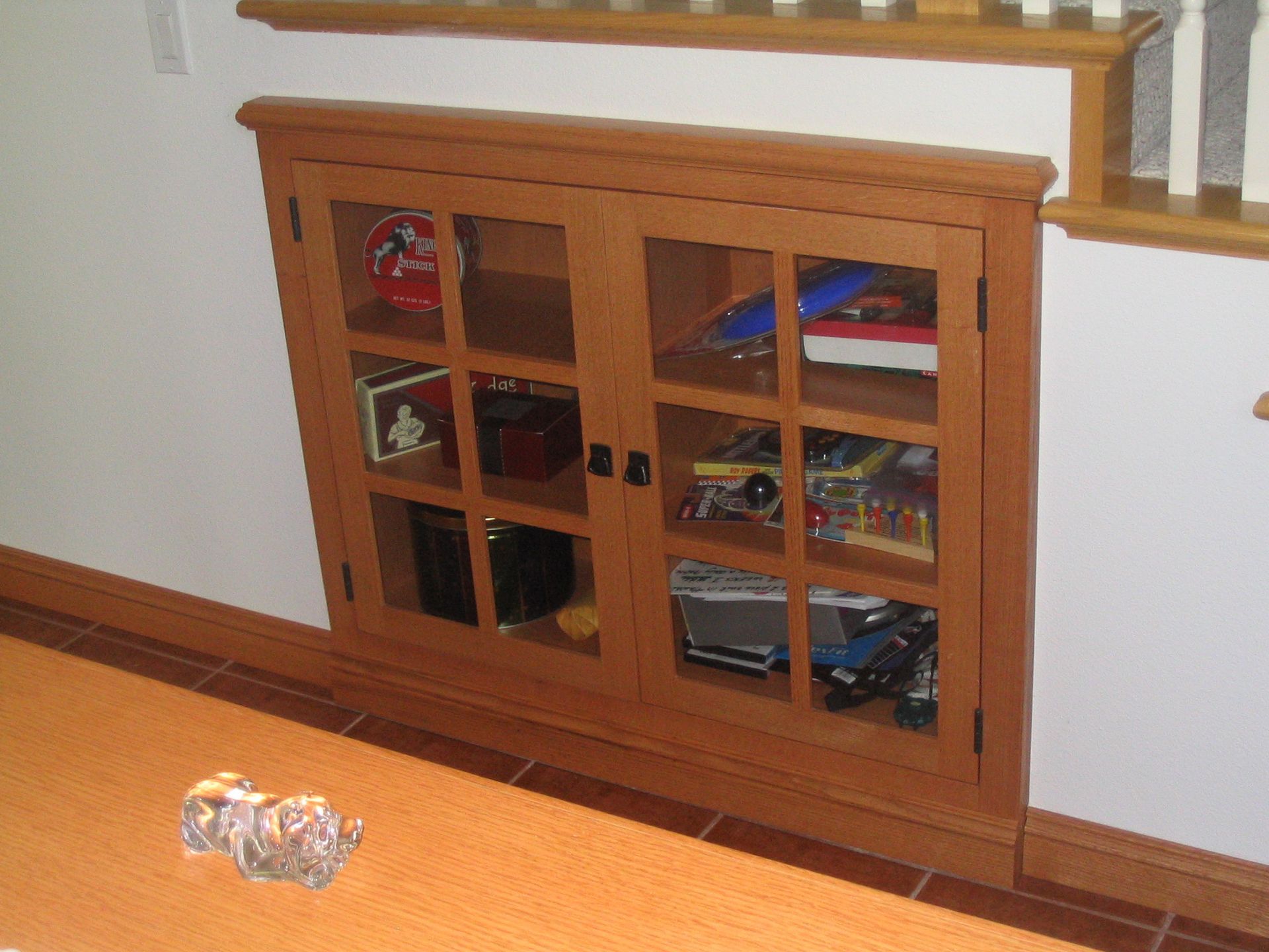 Wooden cabinet built into a wall under stairs, holding toys and games.