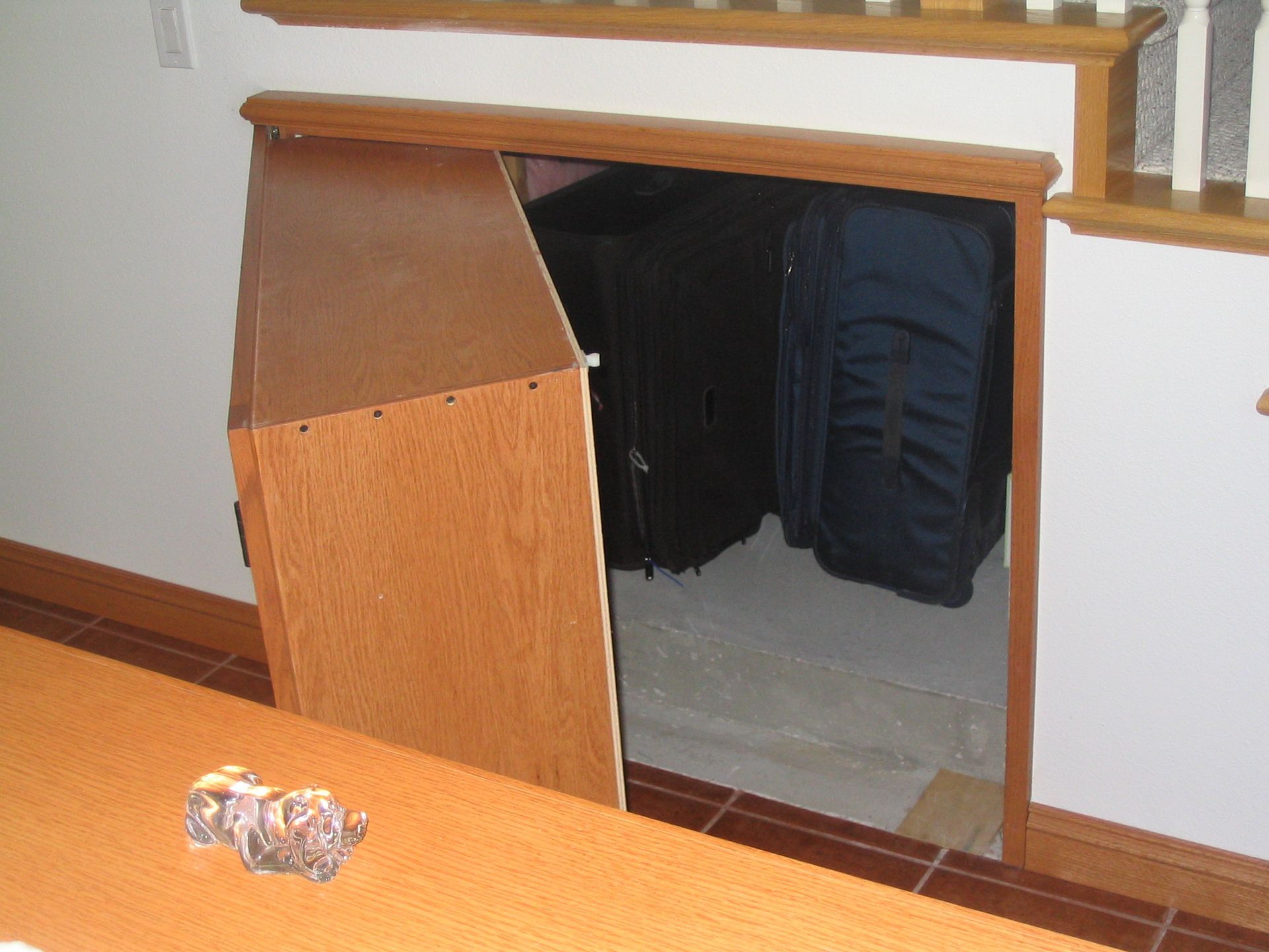 Wooden storage closet under staircase with open door revealing luggage and bags.