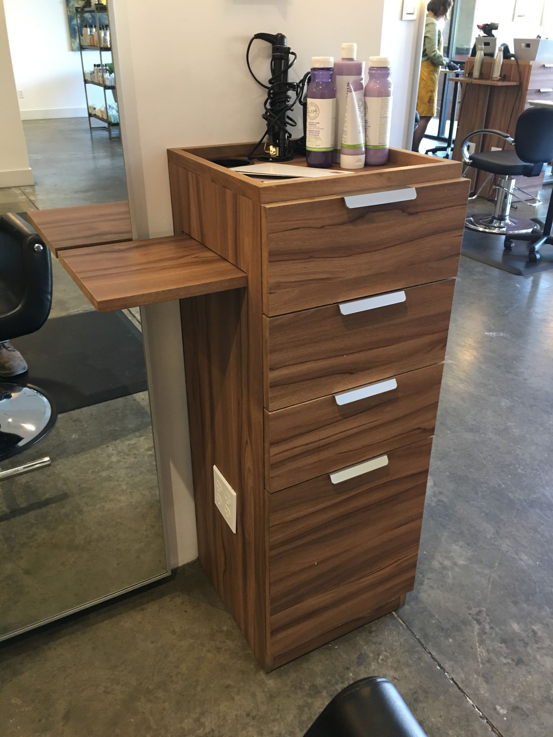 Wooden salon cart with drawers and a pull-out tray, holding hair products.