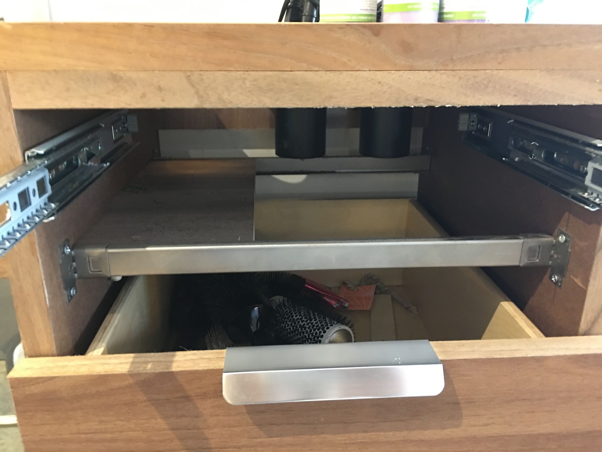 Open wooden cabinet drawer with metal drawer slides and a shelf.
