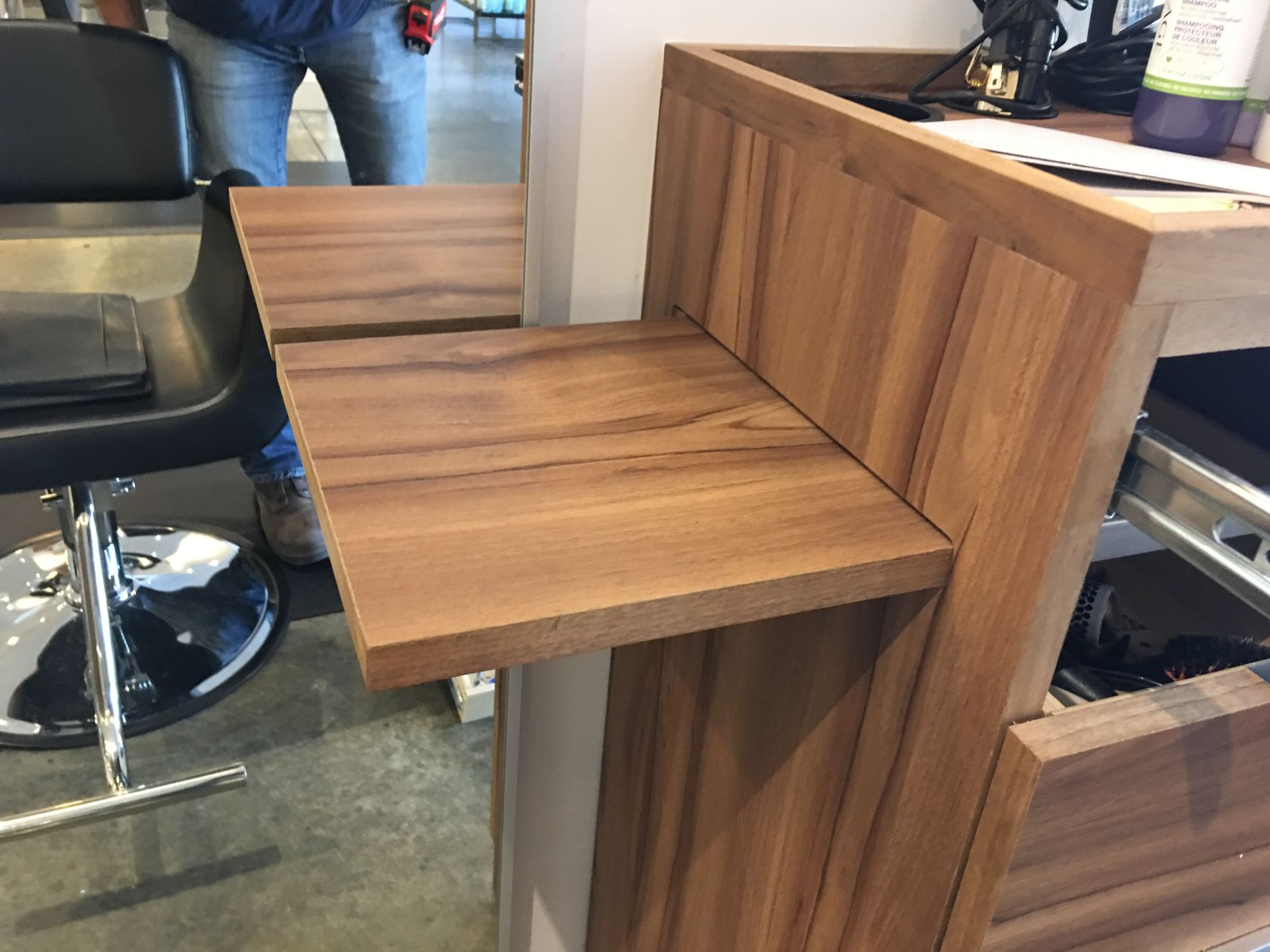Wooden salon station with a fold-out shelf, next to a black salon chair.