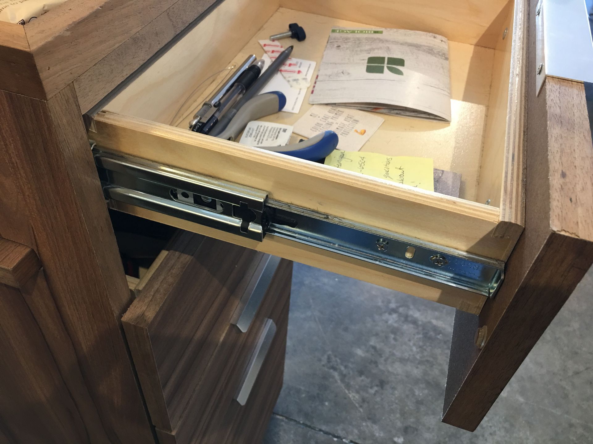 Open wooden drawer with metal slides, containing office supplies and papers.
