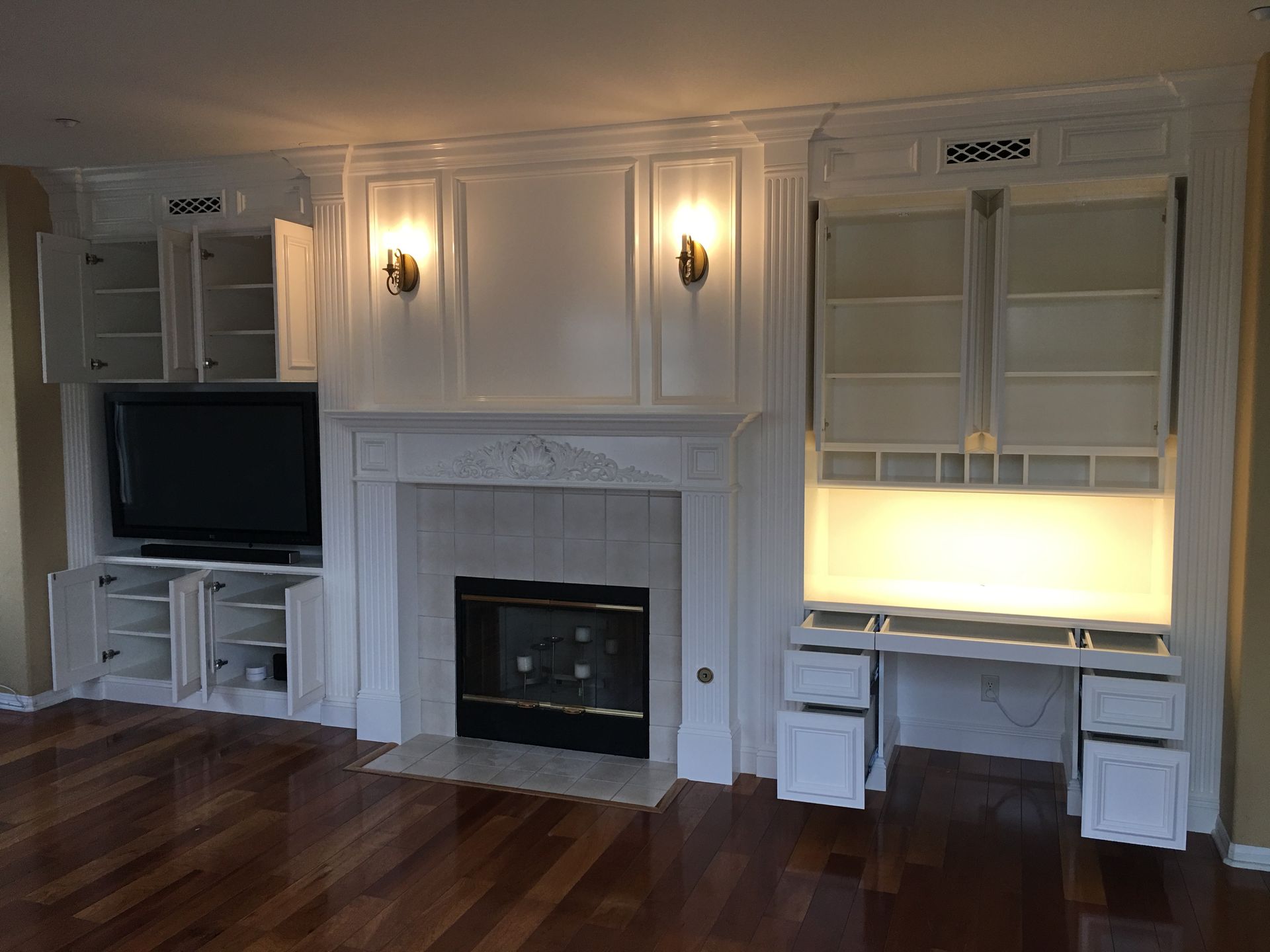 Built-in white cabinets with a fireplace, TV, and desk. Room has wood floors and sconces.