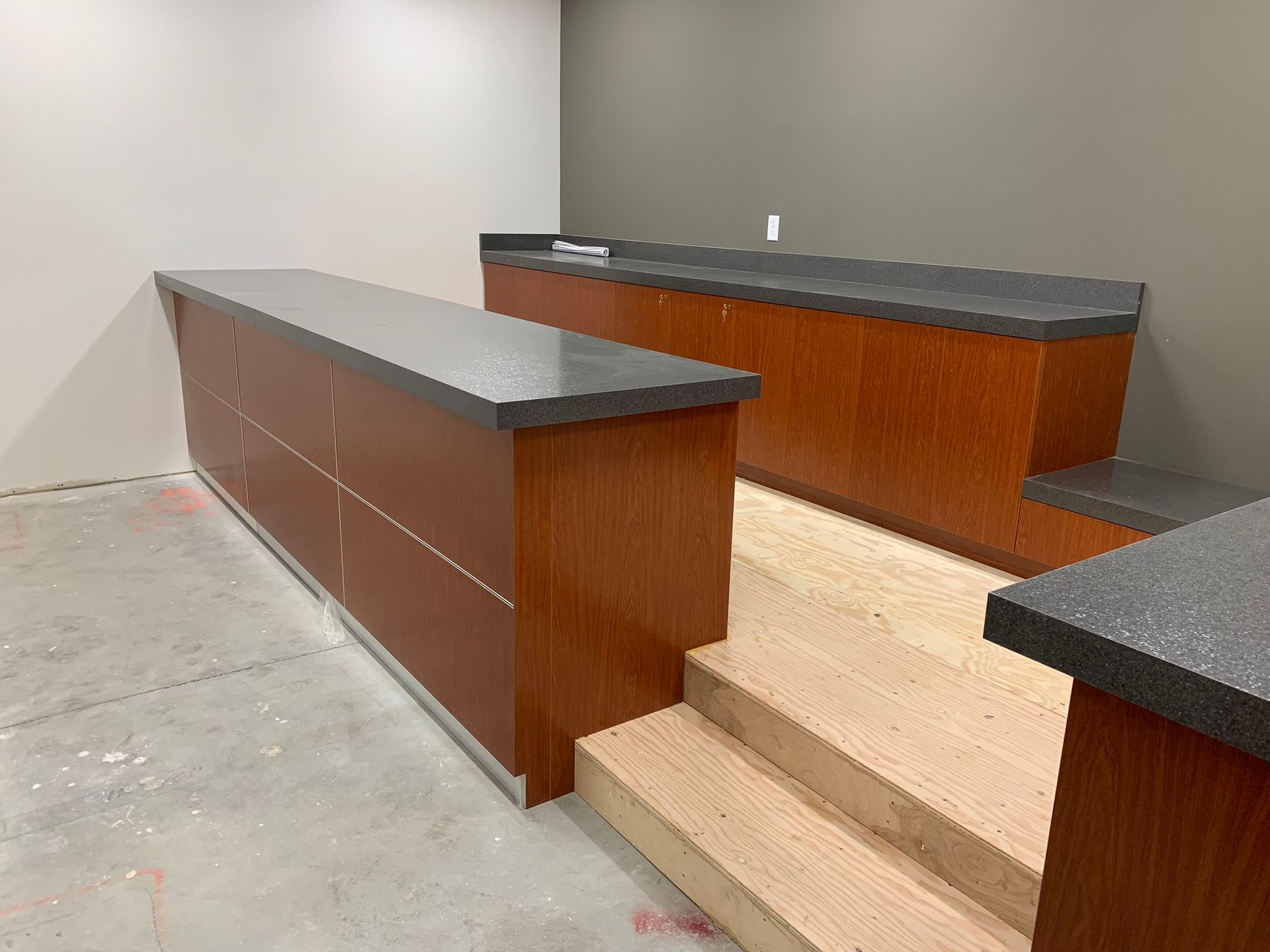 Wooden counters with grey tops in a construction setting with unfinished stairs.