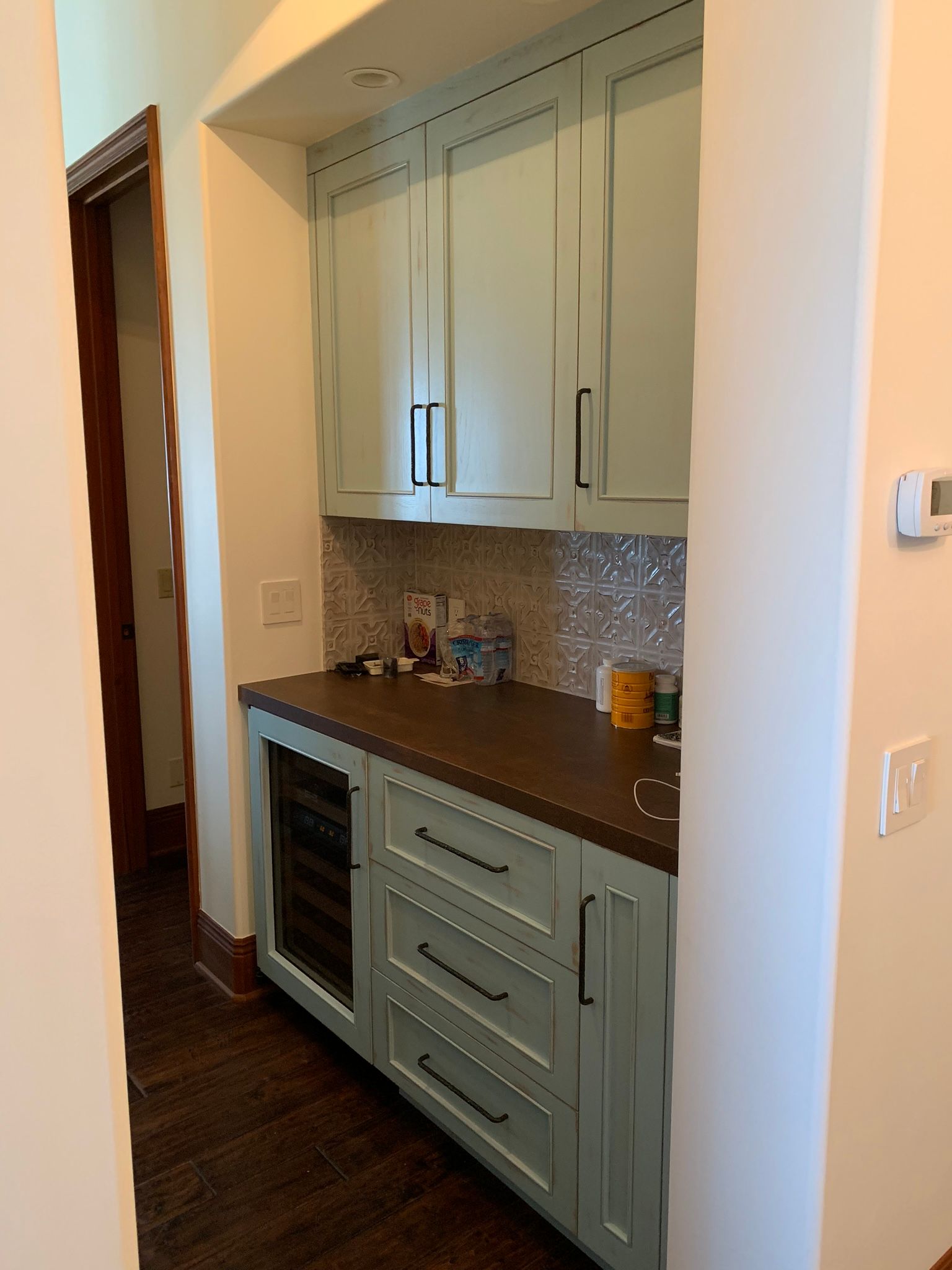 Light blue built-in cabinets with dark countertop, small wine fridge, and mosaic tile backsplash in an alcove.