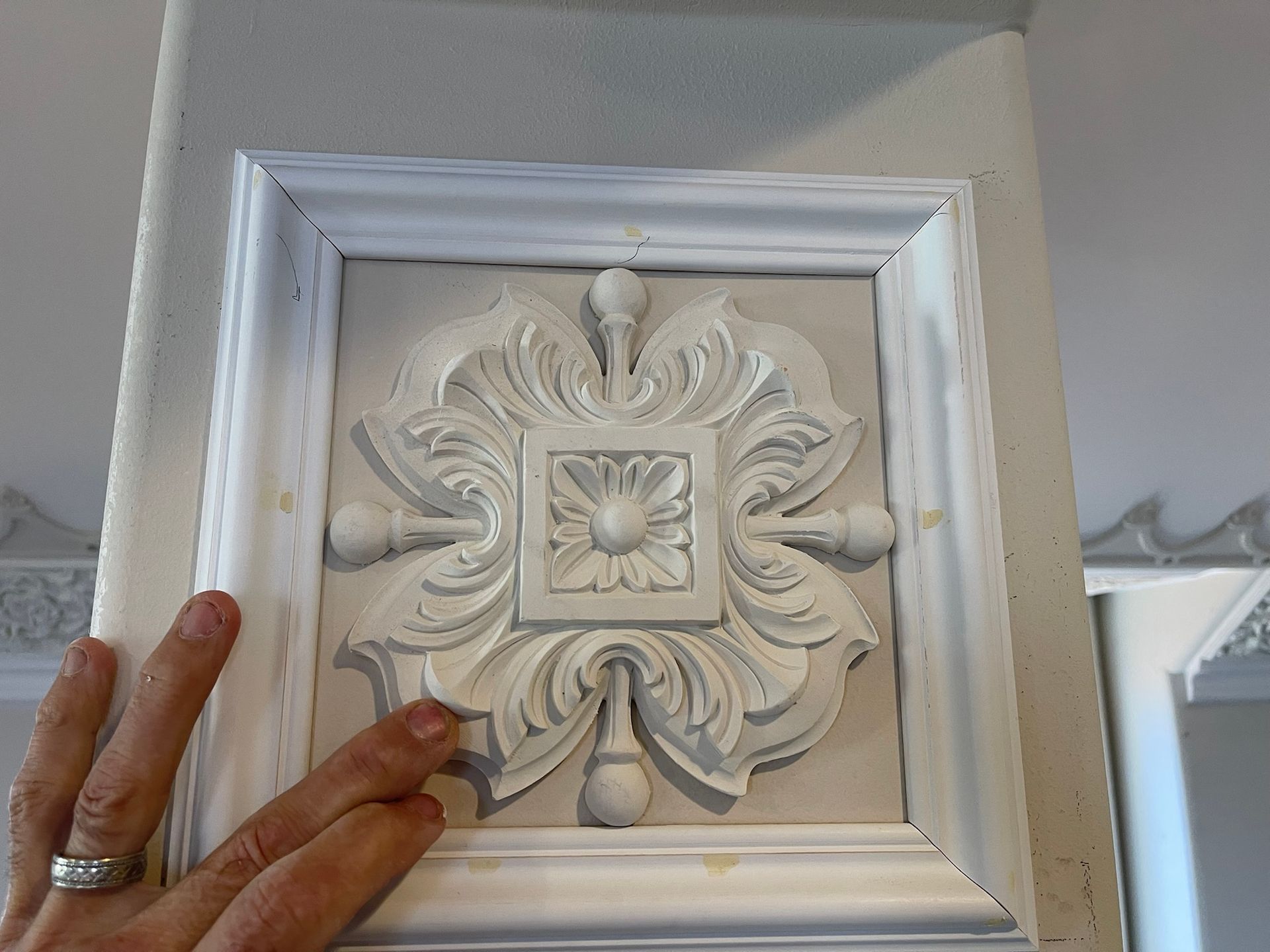 Hand touching a white, ornate decorative wall panel with a floral design.