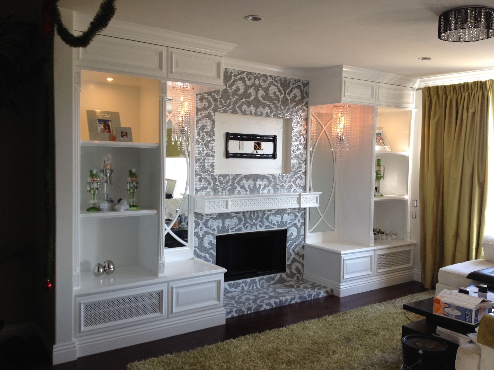 Living room with white built-in shelving, fireplace, damask wallpaper, and gold curtains.