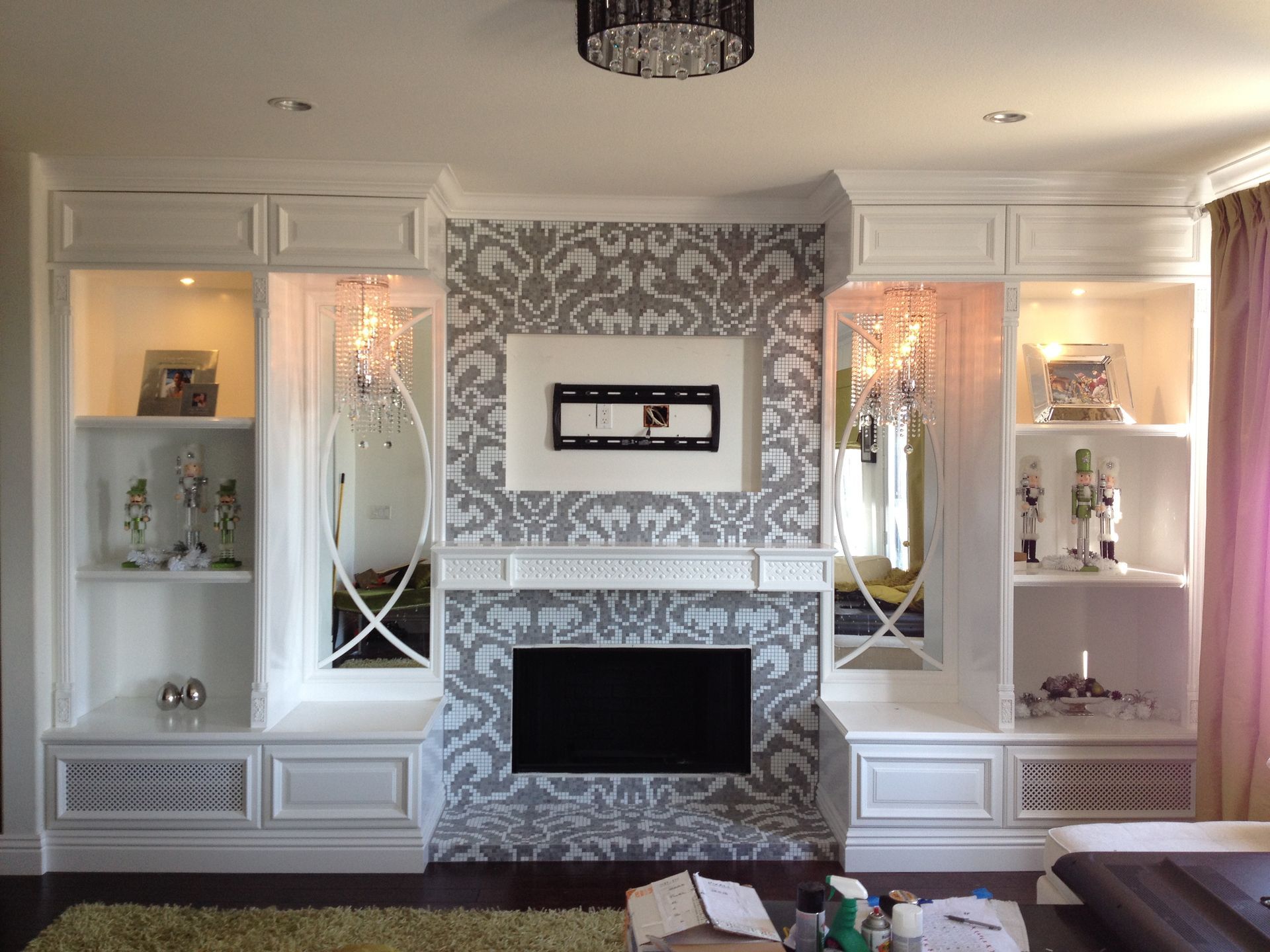 White built-in entertainment center with fireplace, TV, and shelves. Gray patterned wallpaper background.