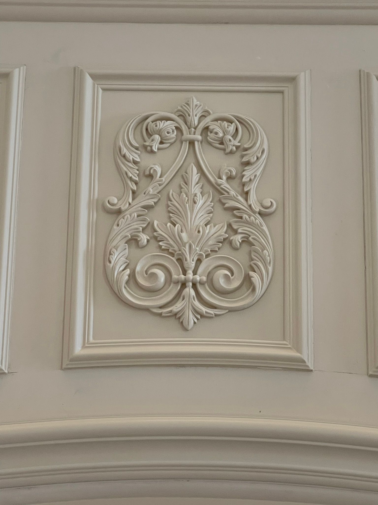 White decorative relief panel featuring an ornate floral design, framed within a larger wall panel.