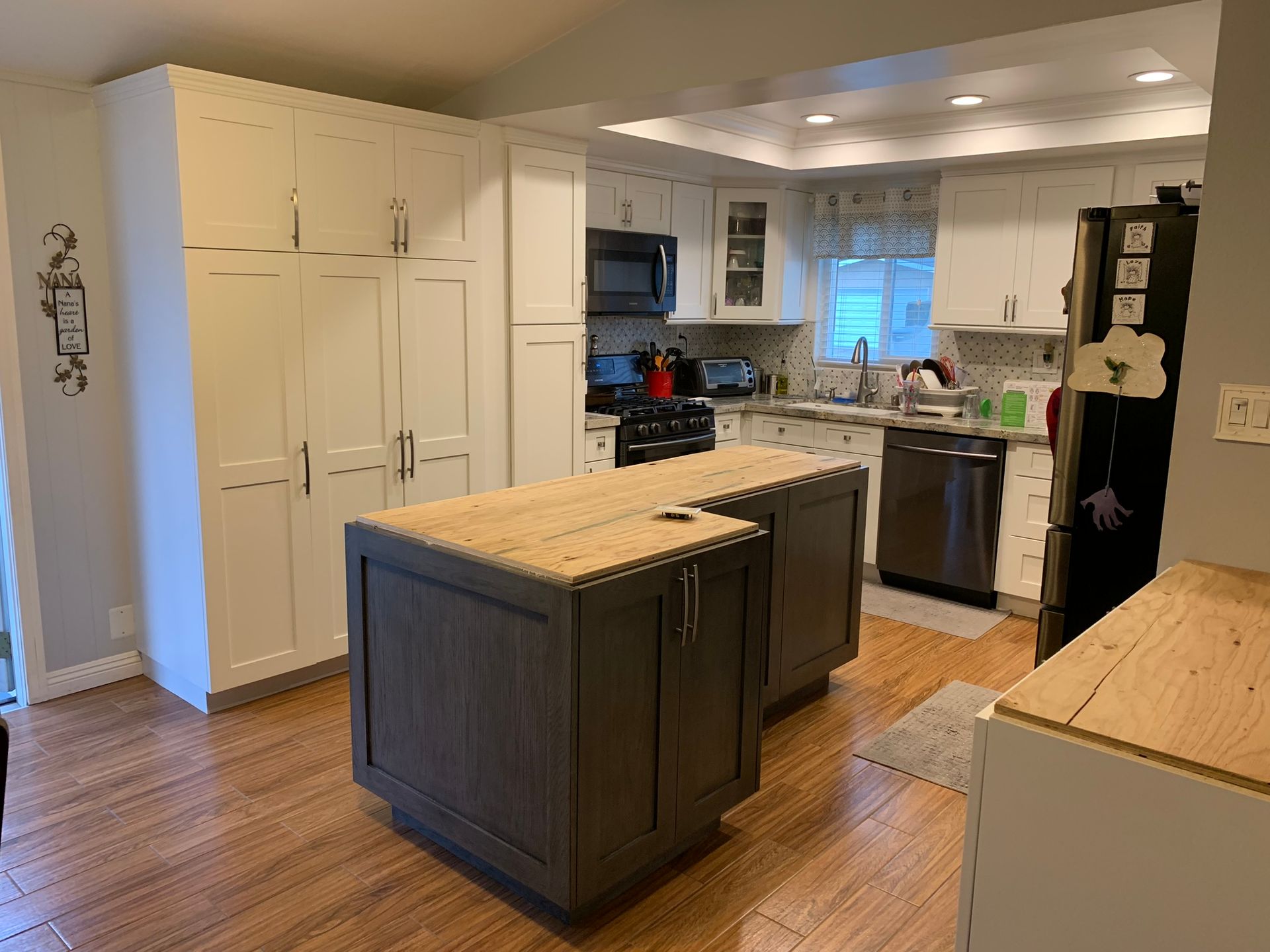Kitchen with white cabinets, dark gray island, wooden countertops, and stainless steel appliances.
