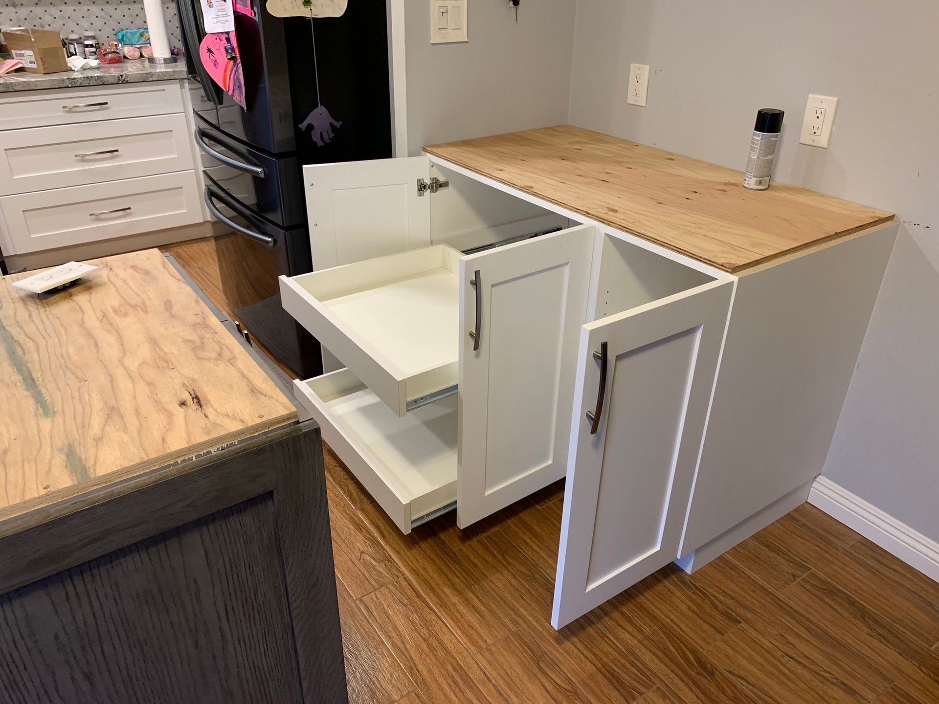 White kitchen cabinet with open doors and pull-out drawers, wood countertop.
