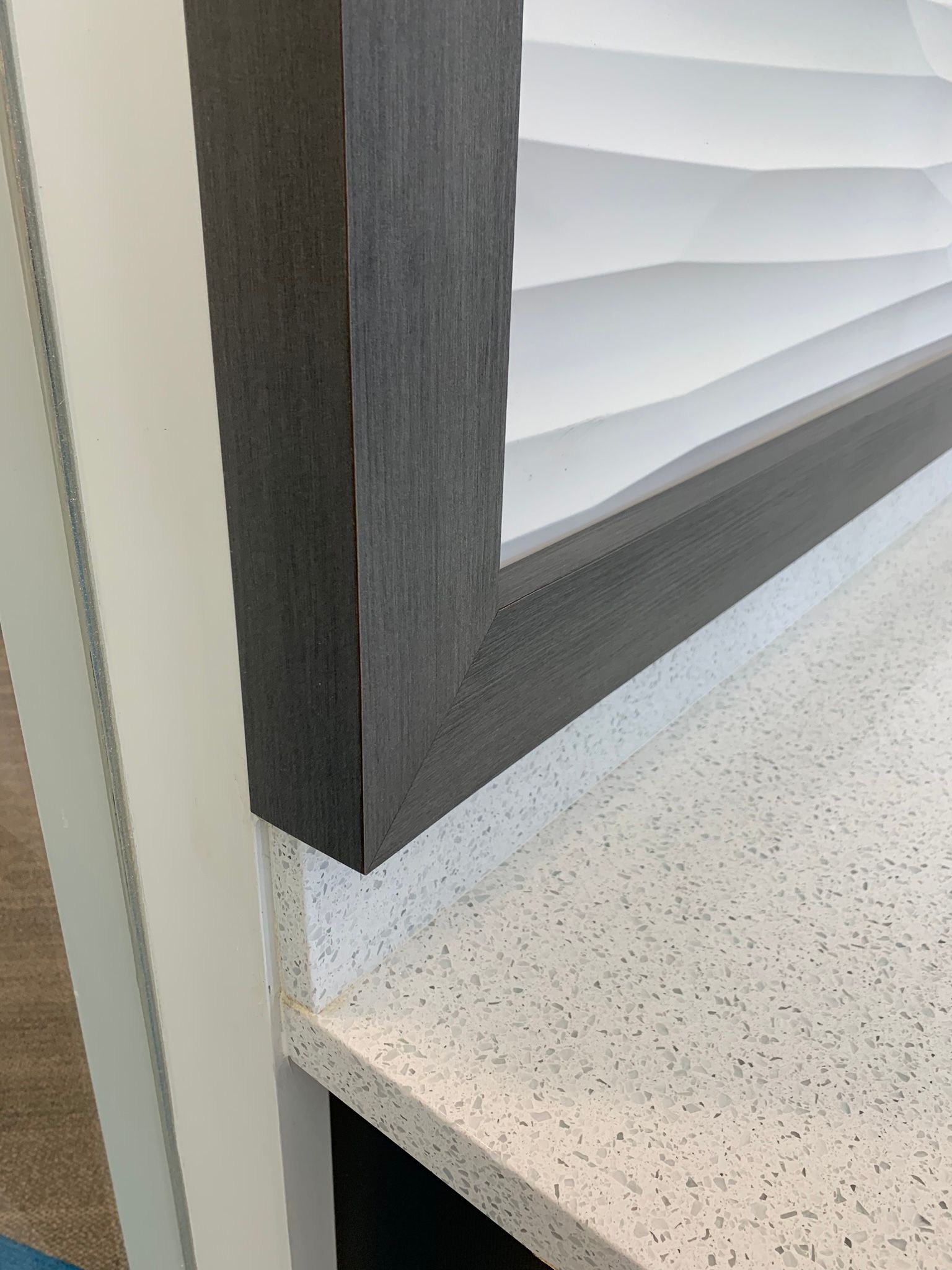 Dark gray framed art piece above a white speckled countertop.