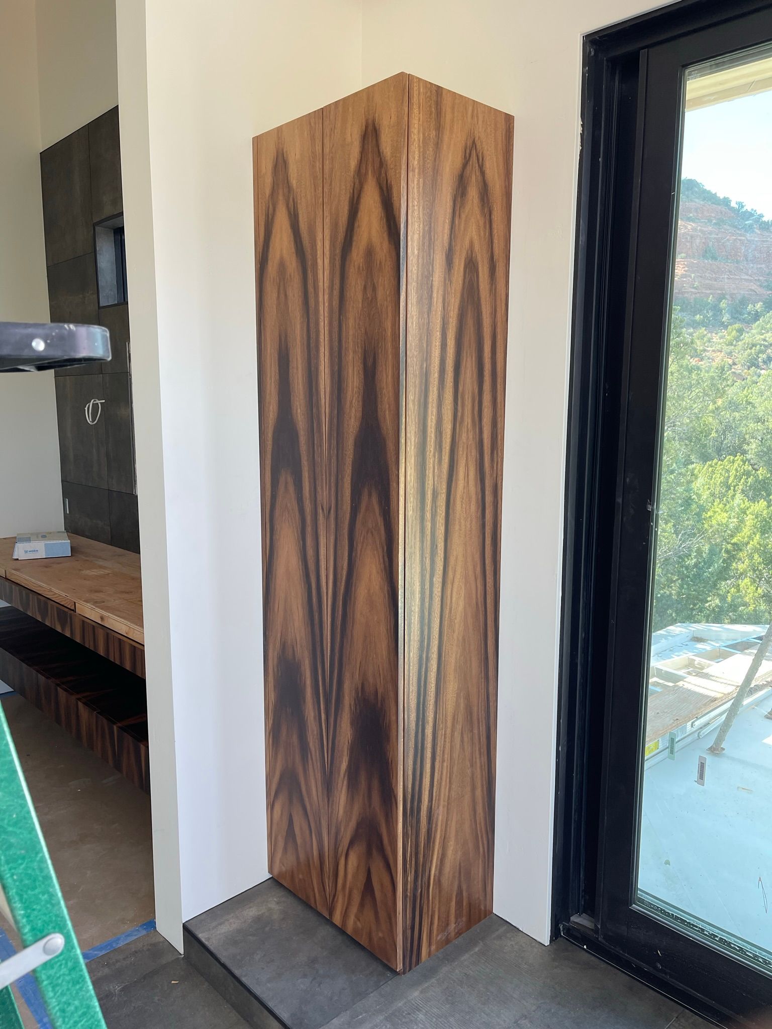 Wood-paneled corner pillar against a white wall, next to a black-framed window.