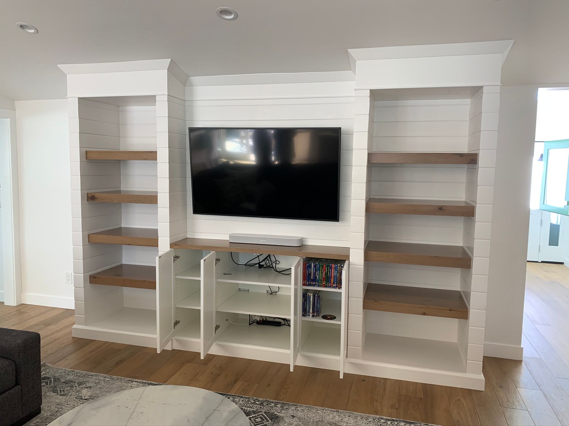 Built-in white shelves with a TV in the center and lower cabinet doors, all against a white paneled wall.