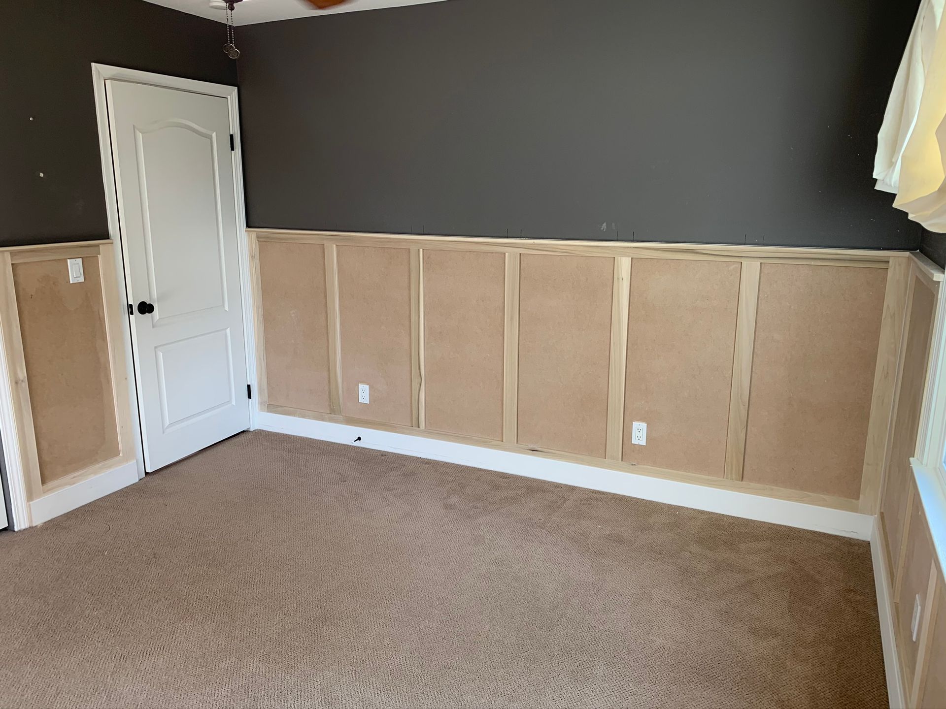 Bedroom with partial wood paneling, white door, gray wall, and beige carpet.