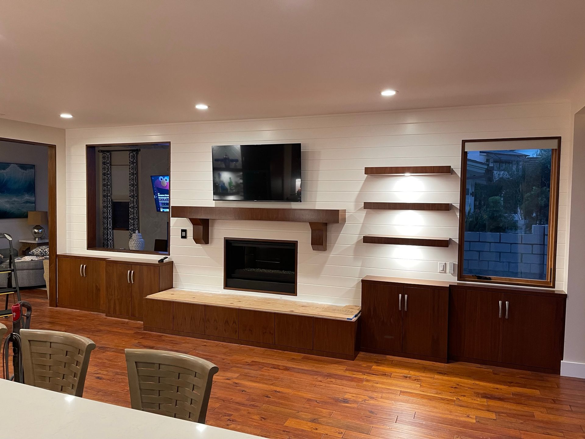 Living room with fireplace, TV, and built-in wooden cabinets. White brick wall, wooden shelves, and hardwood floors.