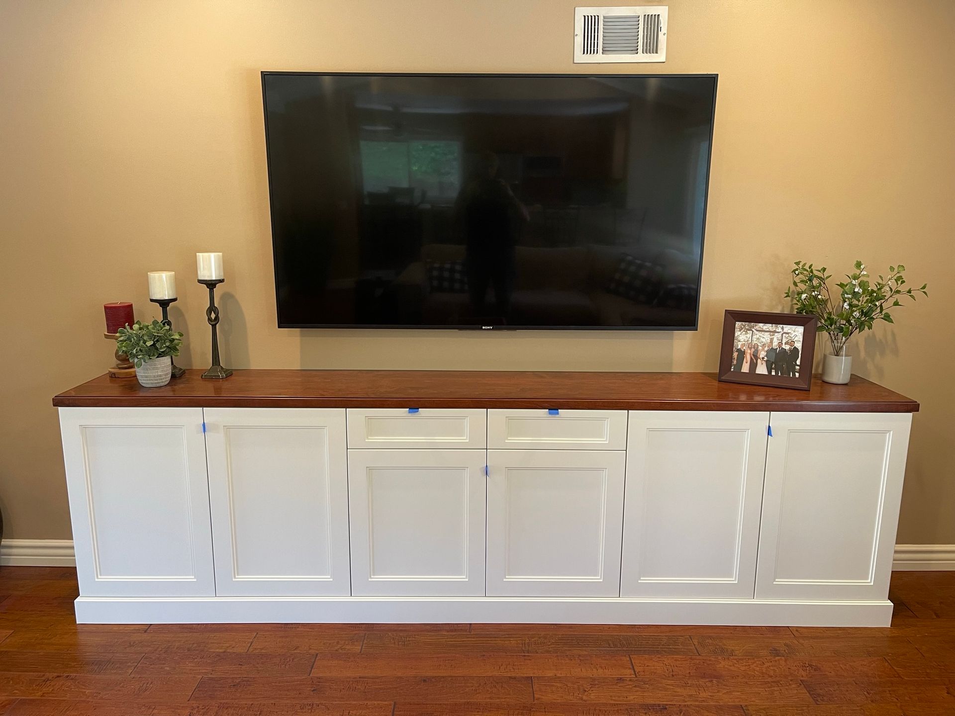 White cabinet with wood top, supporting a mounted TV. Decorative items on top.