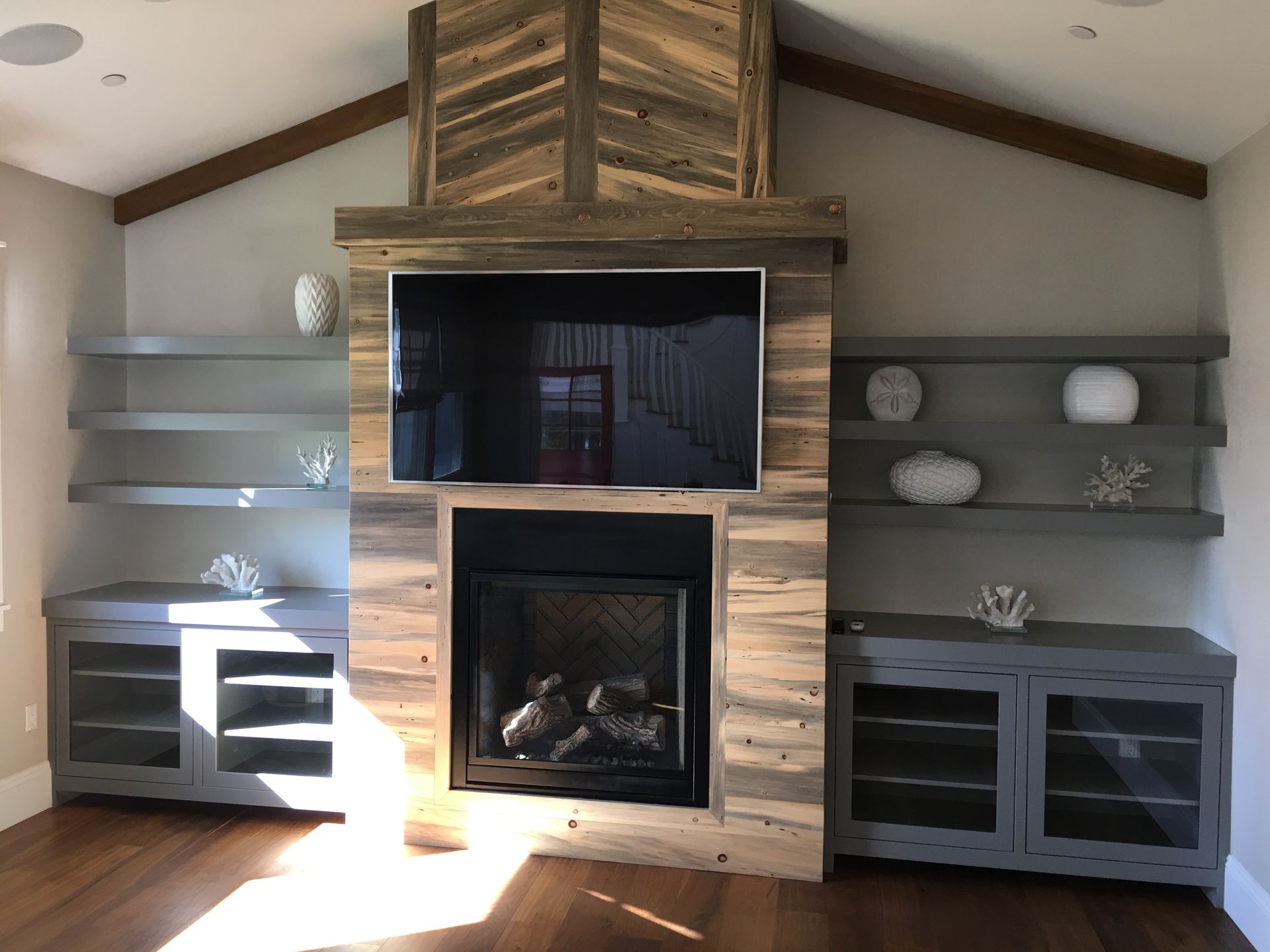 Fireplace with TV and built-in shelves. Reclaimed wood surround, gray cabinets, white decorative objects.