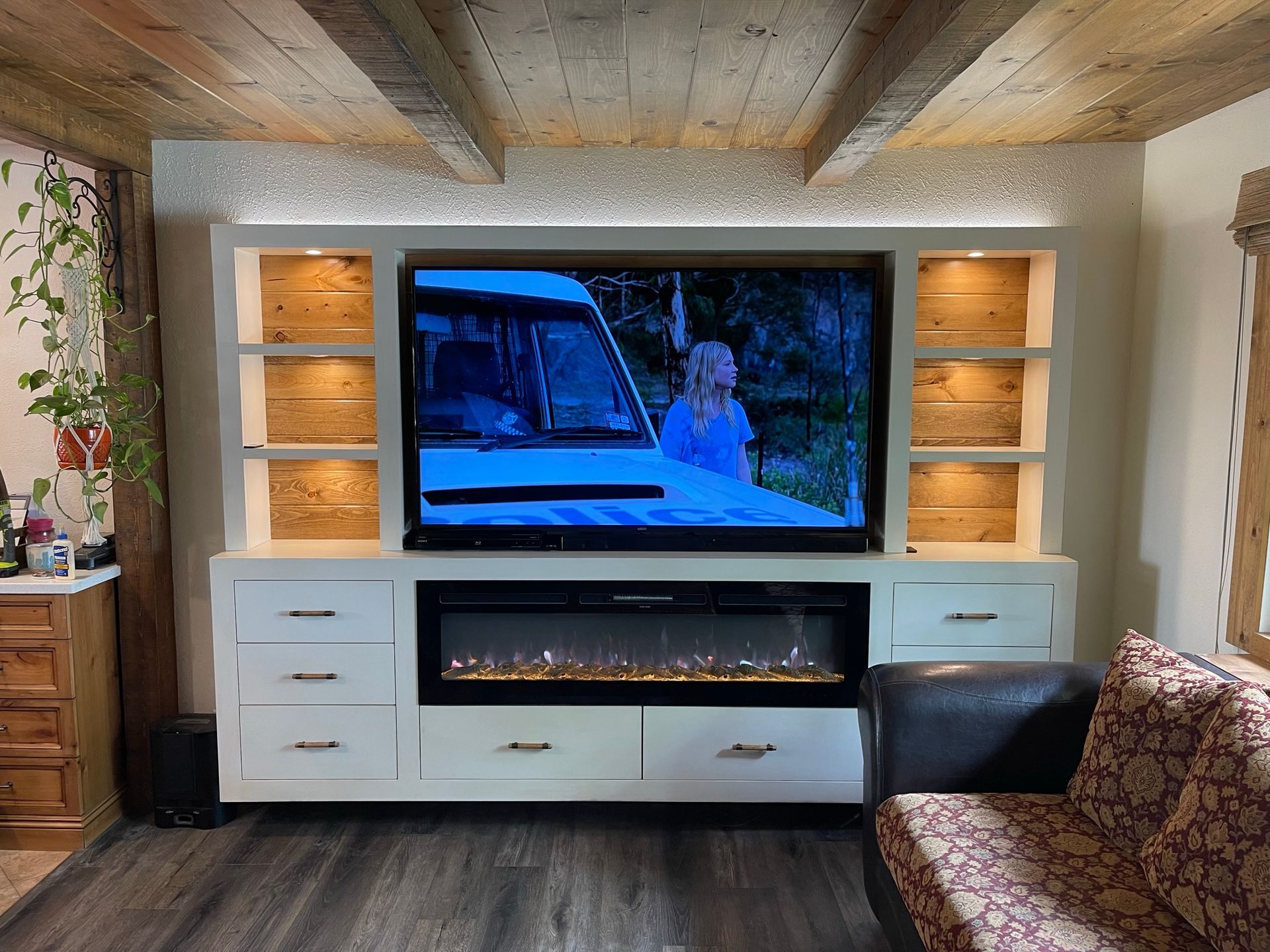 Entertainment center with a TV, fireplace, shelves, and built-in lighting.