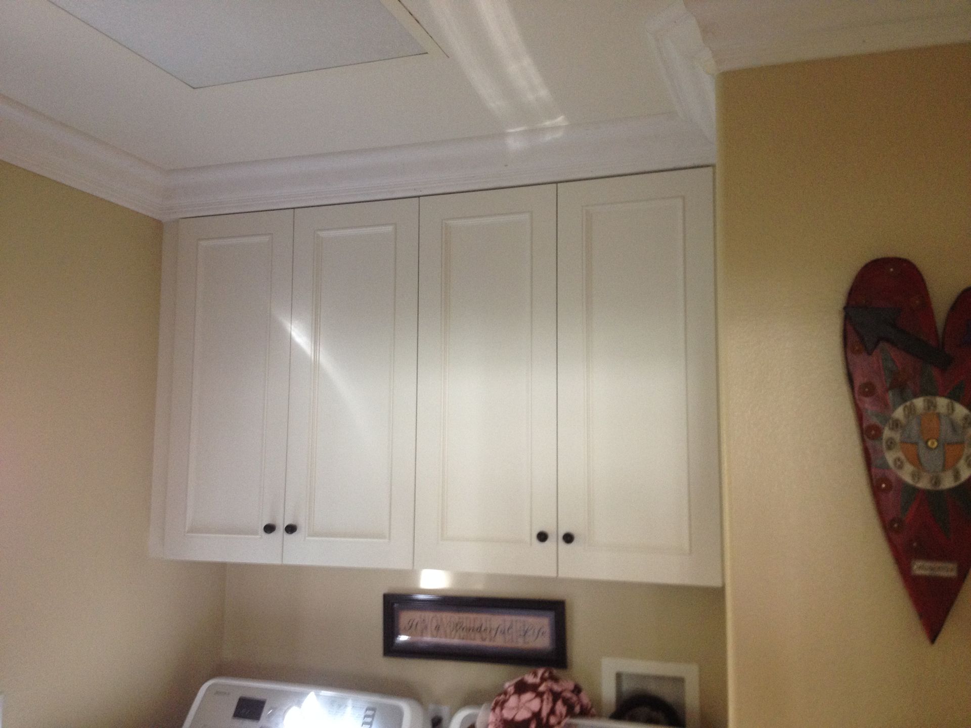White cabinets with black knobs above a washing machine in a laundry room; heart decor on wall.