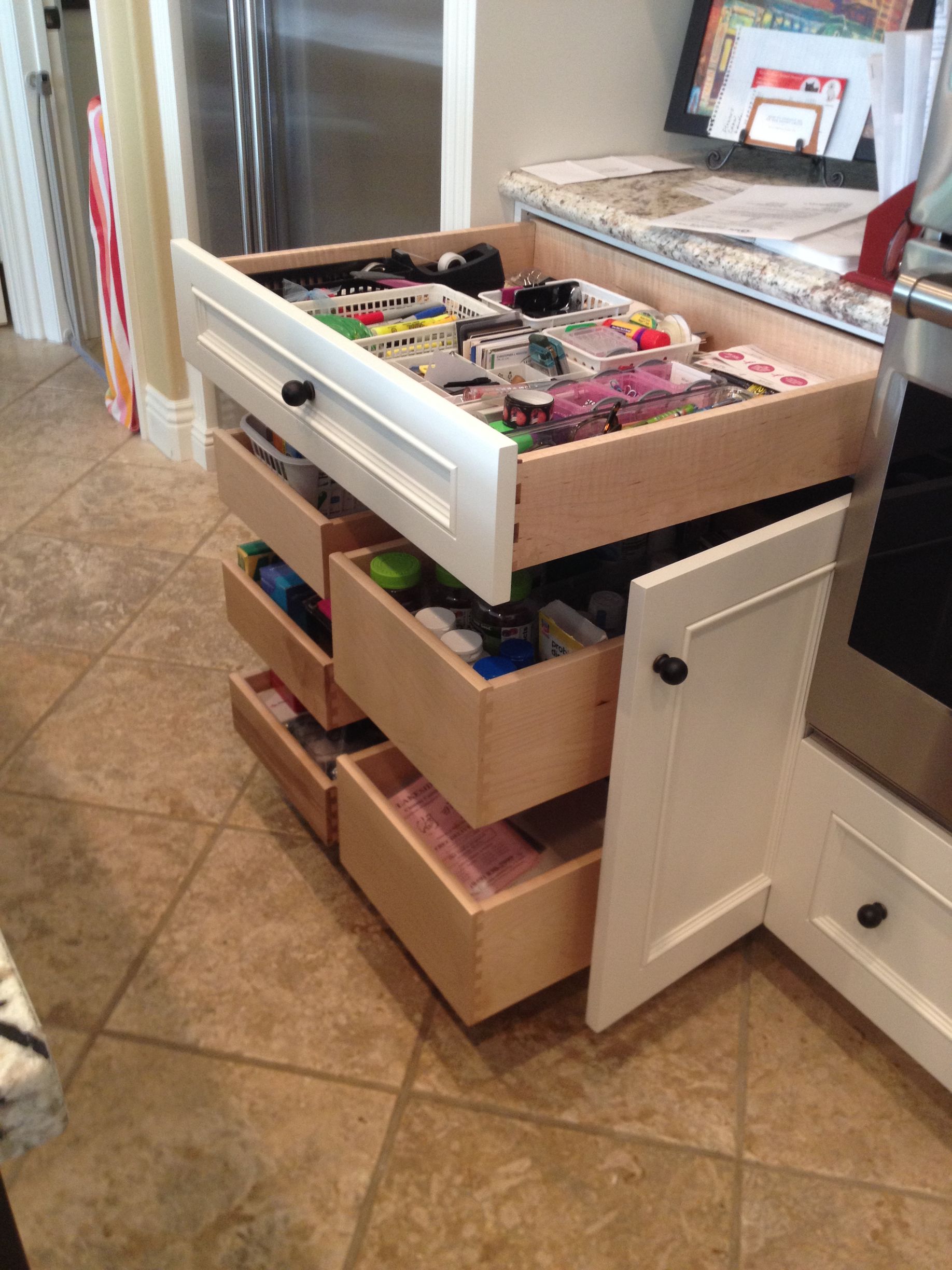 White kitchen cabinet with multiple pull-out drawers, one open and filled with contents.