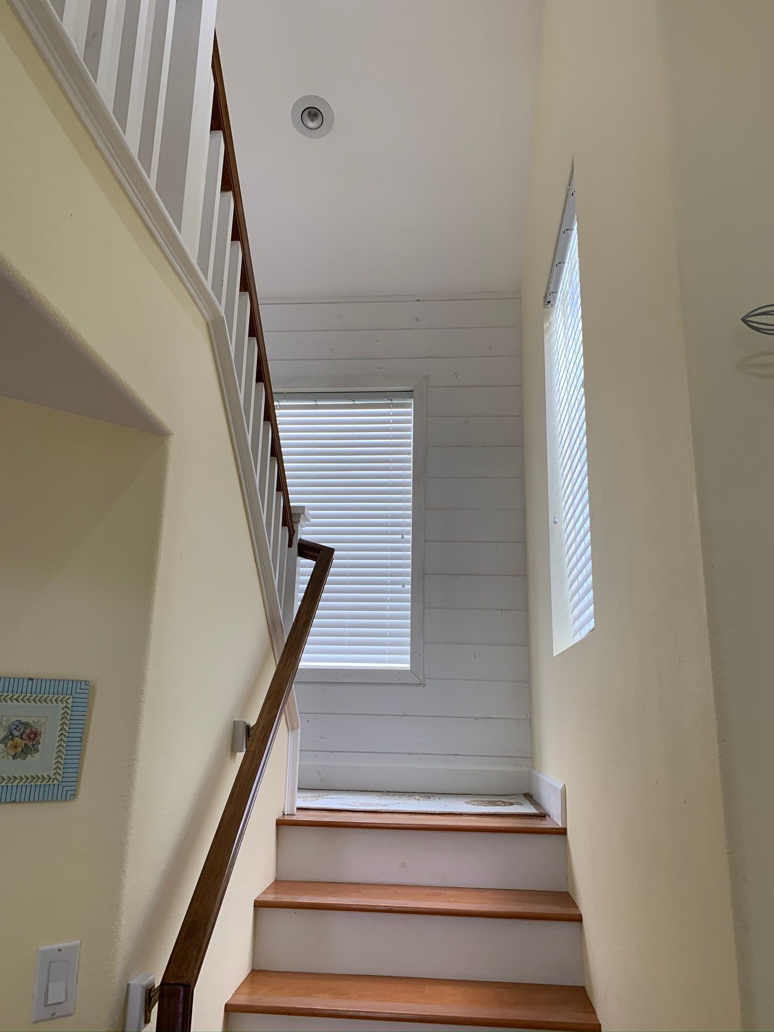 Staircase with wooden steps, railing, and a window with blinds; white wall paneling.