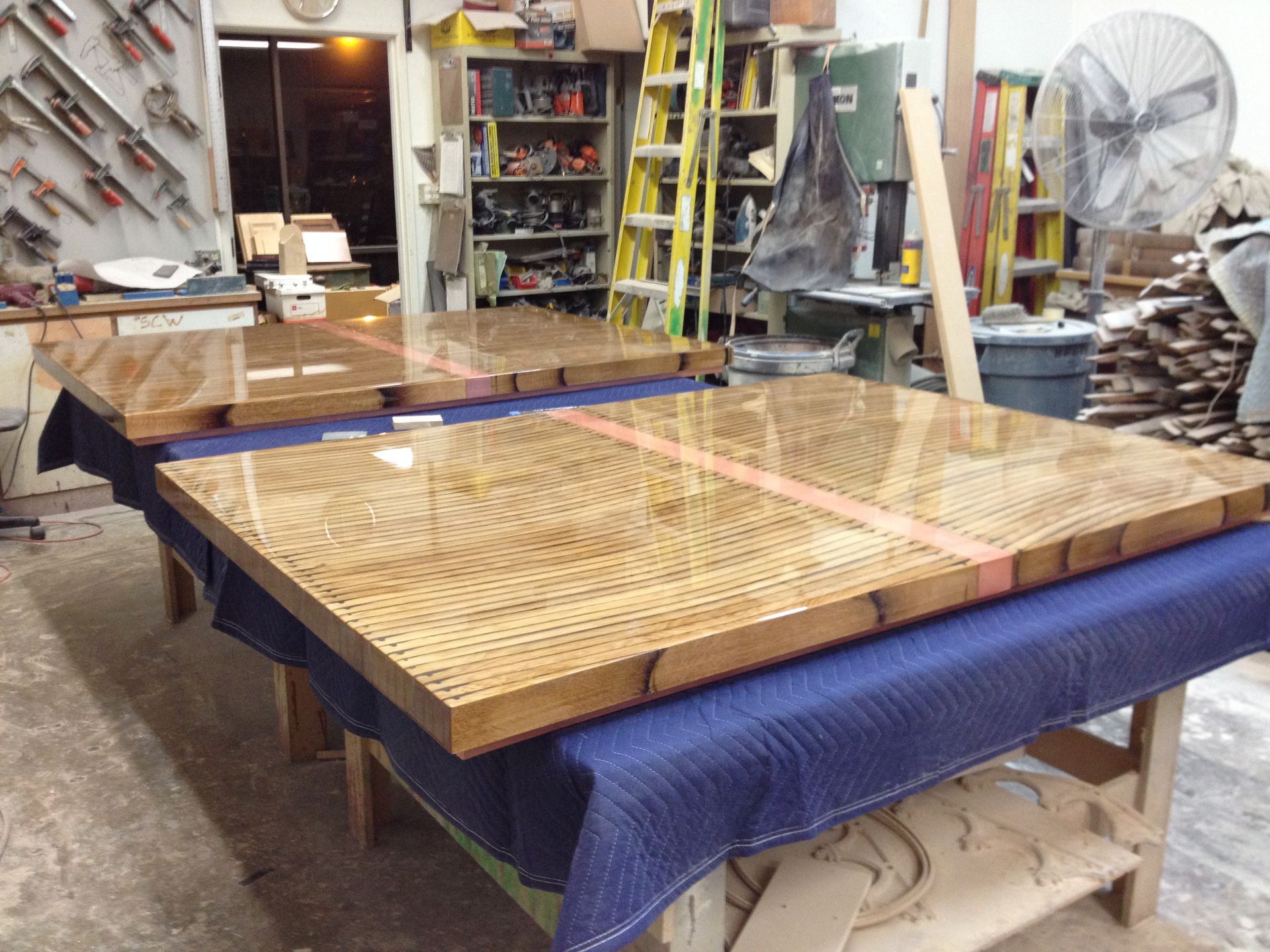 Two large wooden tabletops with a glossy finish on a workbench.