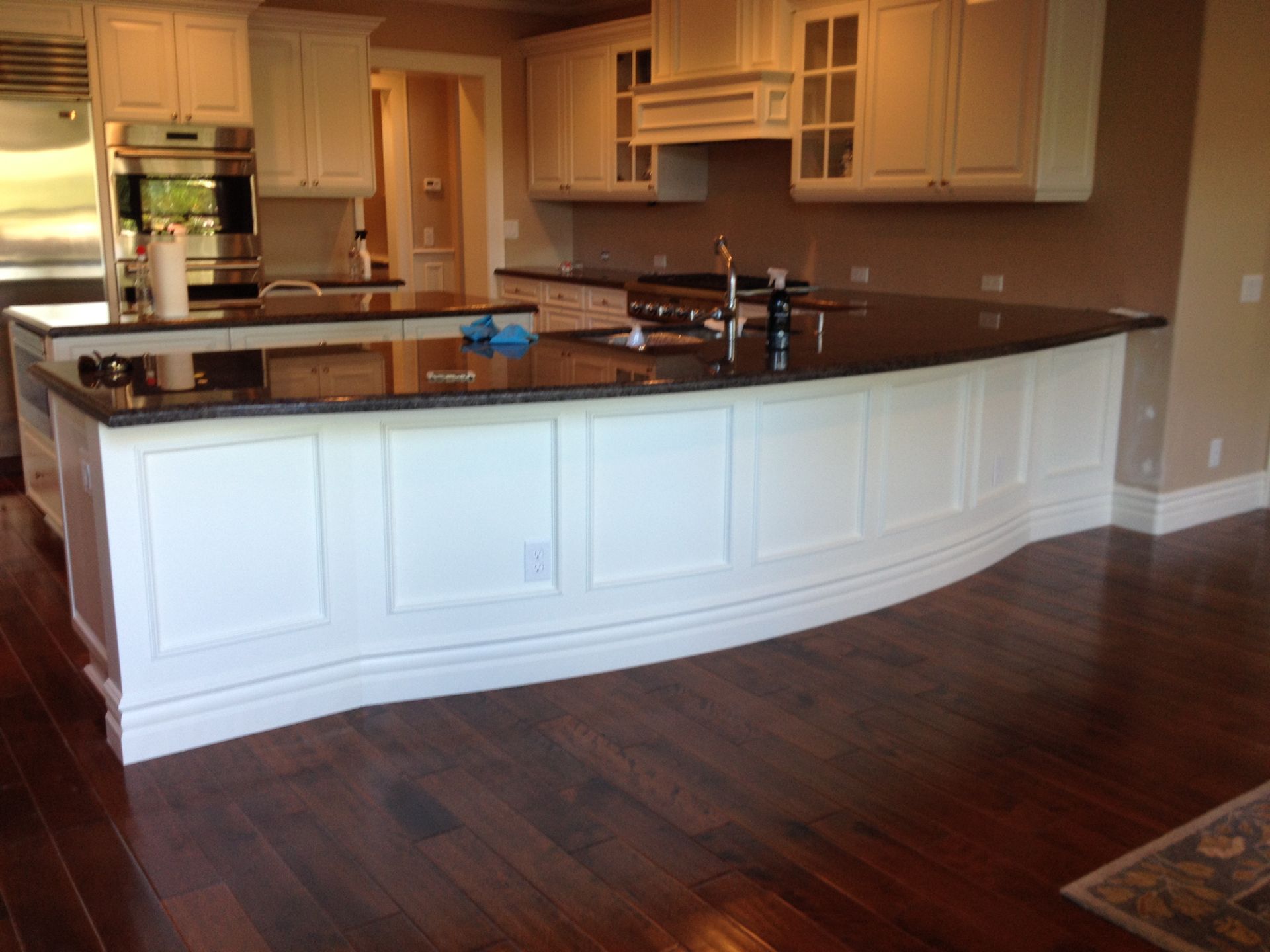 White kitchen with dark granite countertop island and hardwood floor.
