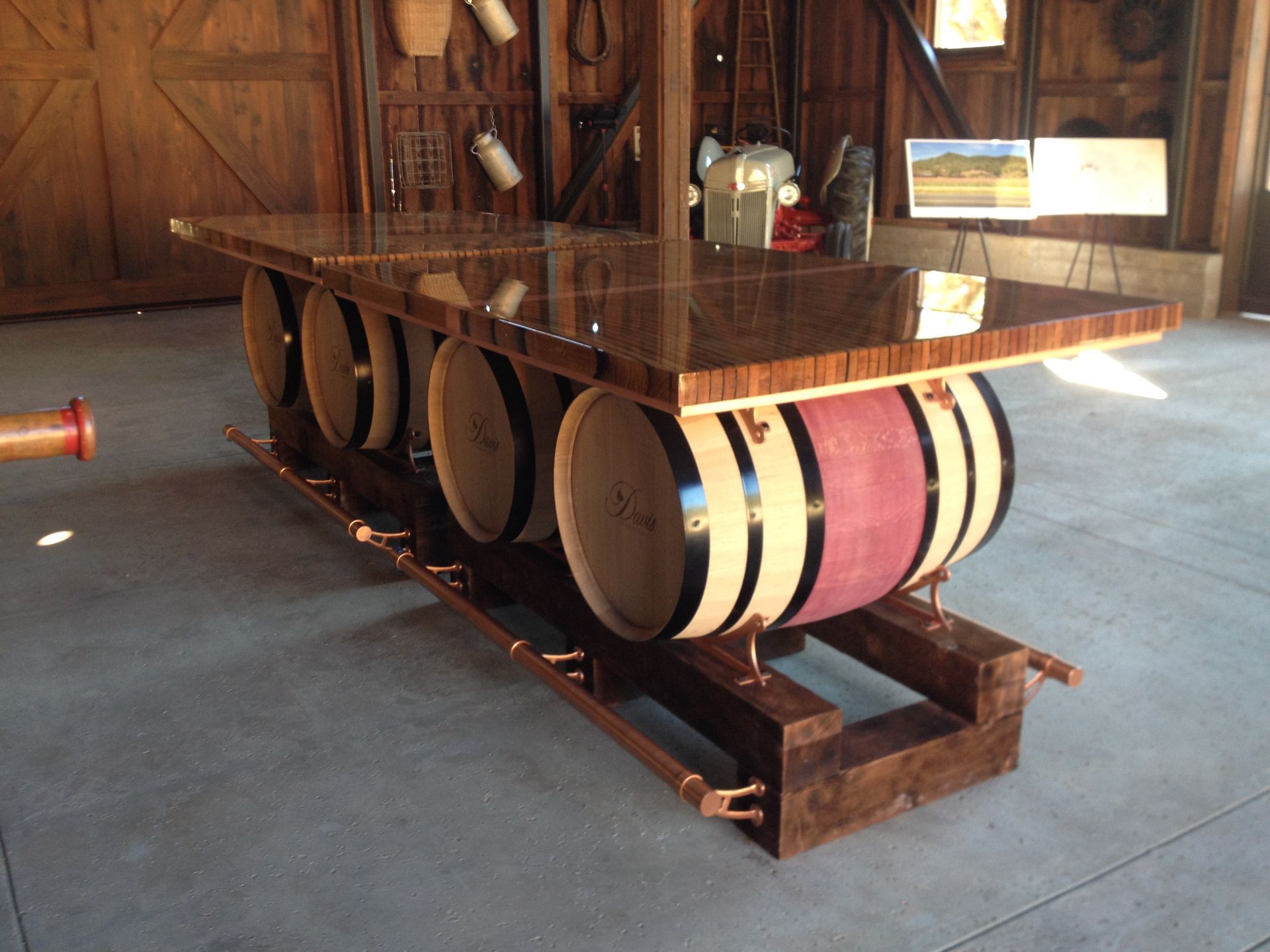 Bar table with wooden barrels as supports, copper accents, and a dark brown surface in a barn.