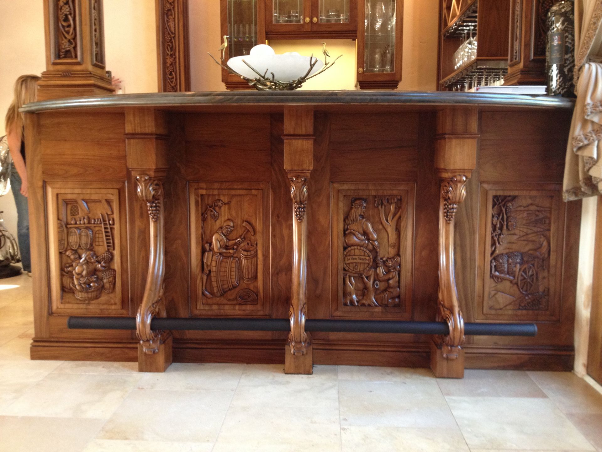 Wooden bar with carved panels, dark countertop, and footrest.