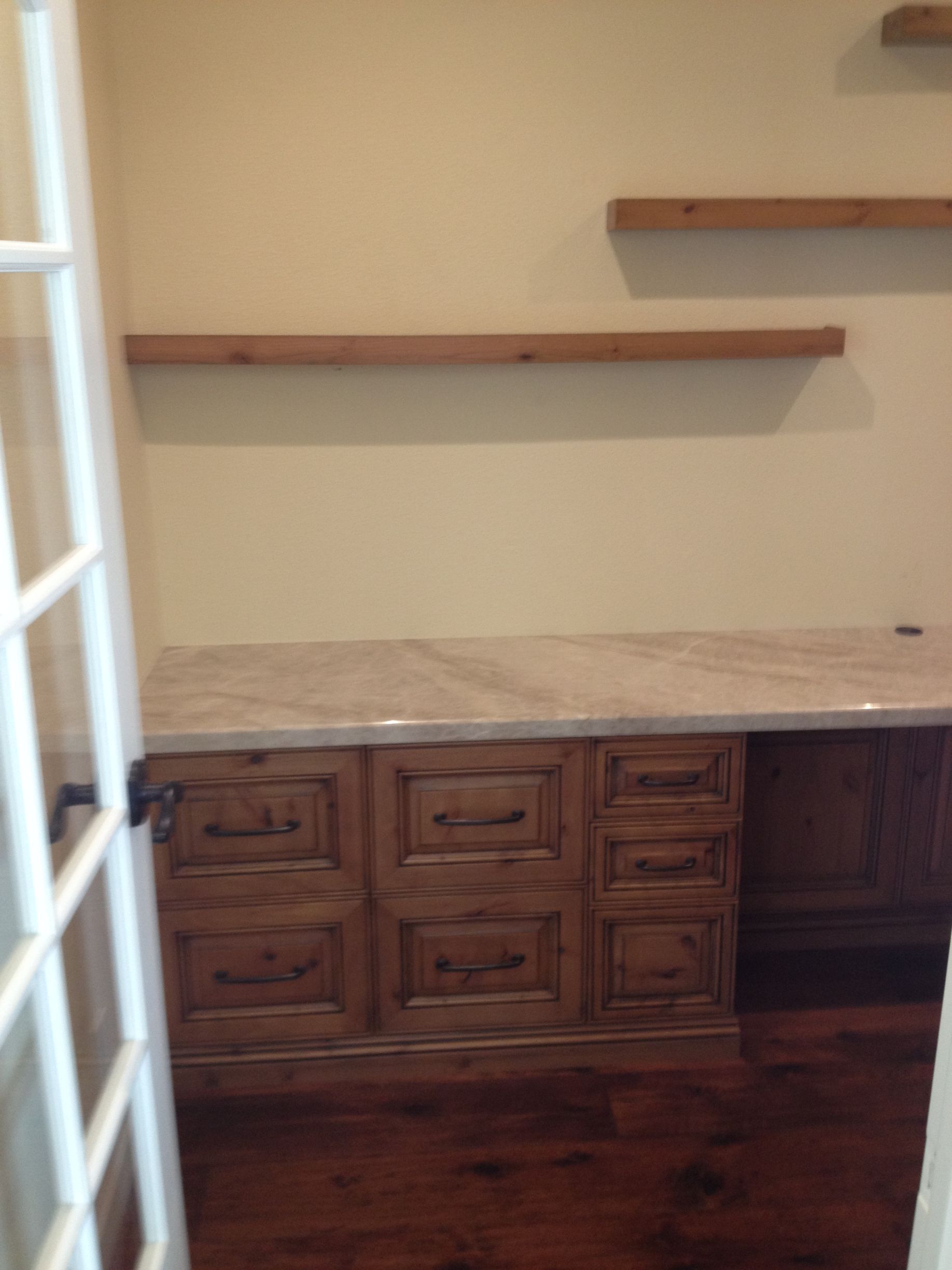 Wooden desk with drawers and marble top, with two wooden shelves above.  Door on the left.