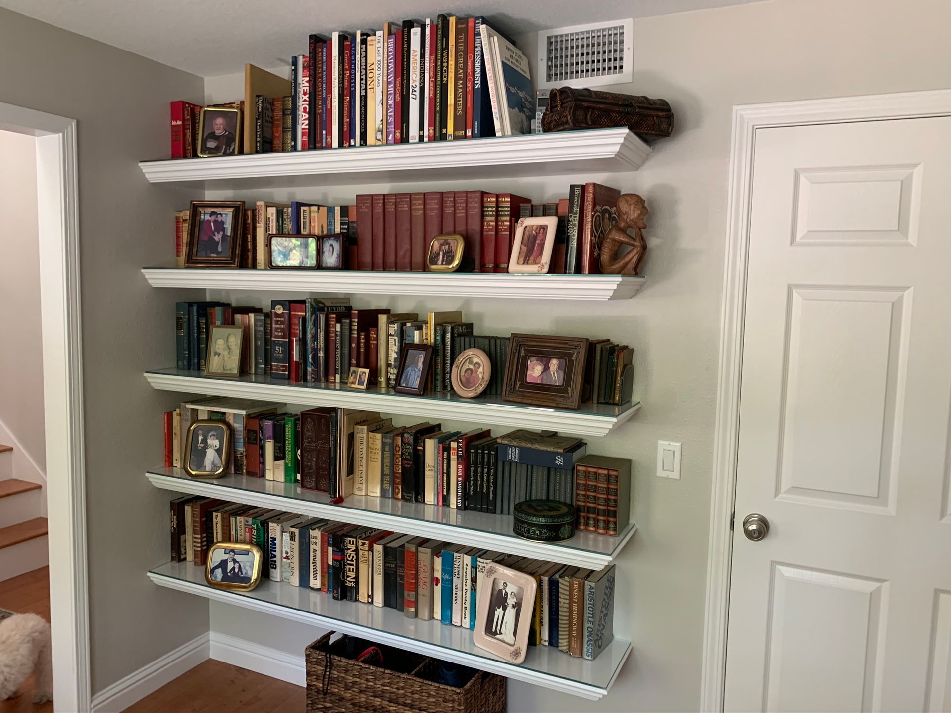Bookshelves filled with books and decorative items on a light grey wall next to a white door.