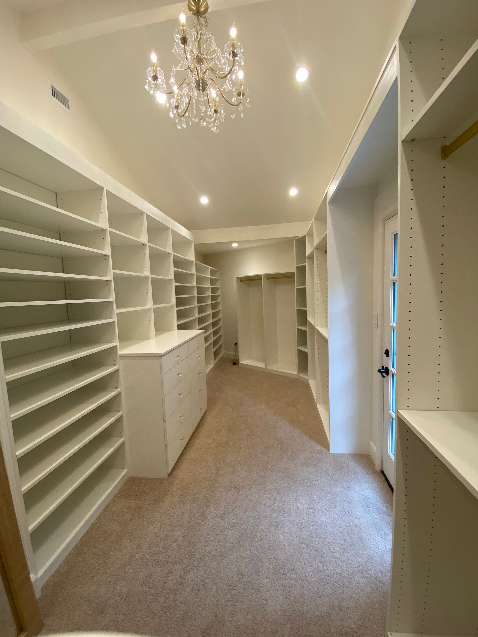 Empty, white walk-in closet with shelves, drawers, and hanging rods; wood flooring.