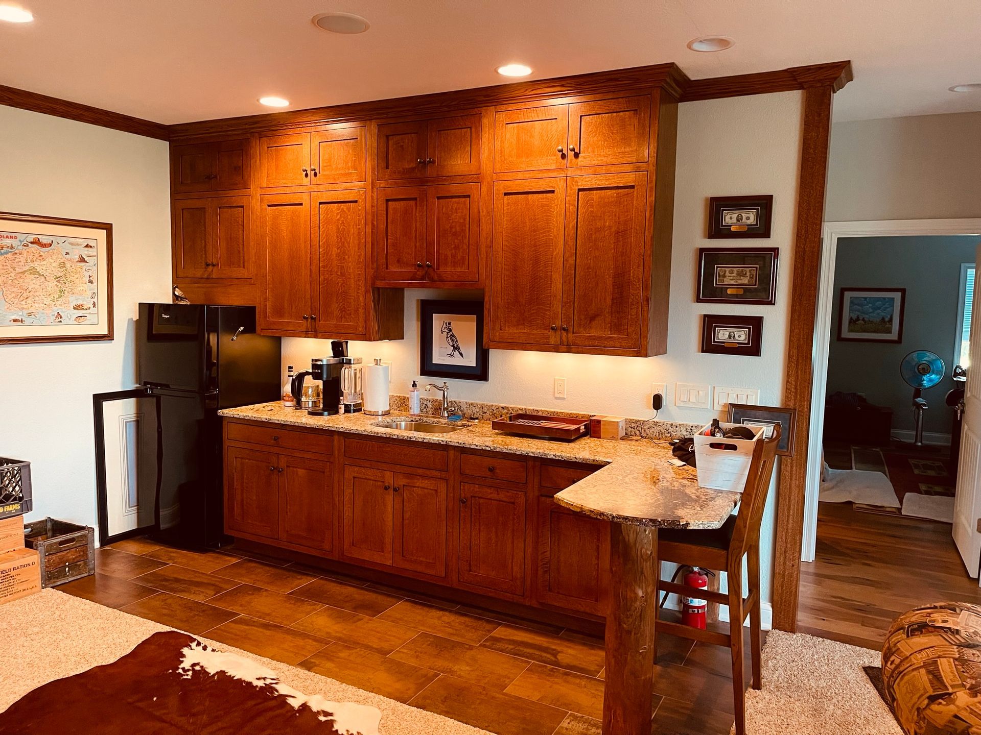Kitchenette with wood cabinets, black refrigerator, granite countertop, and small bar.