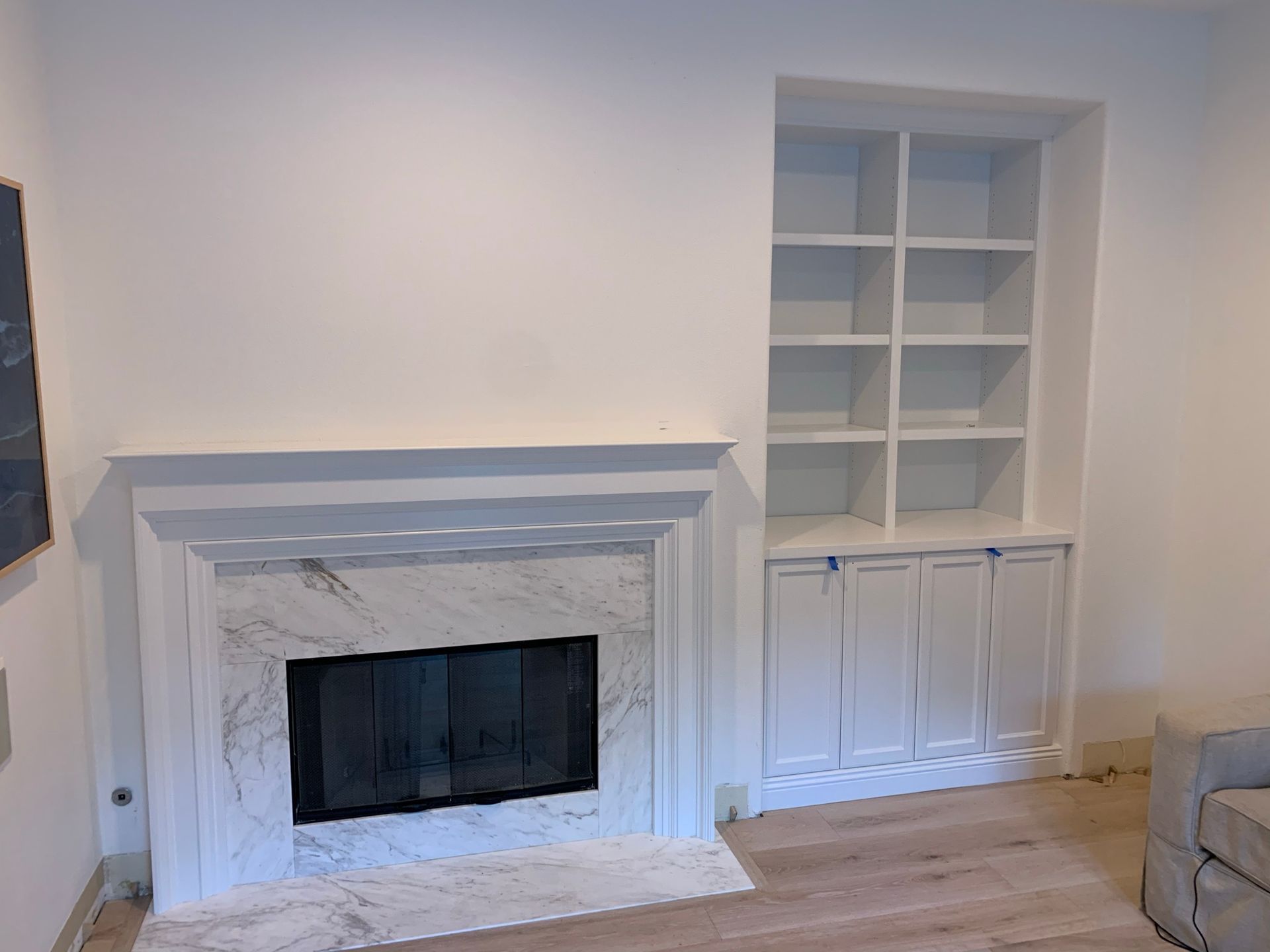 White fireplace with marble surround, built-in white bookshelves, and light-colored wood flooring.