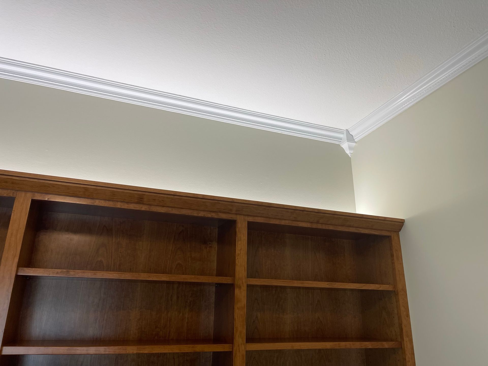 Bookshelves under a white ceiling with decorative crown molding in a room with light beige walls.