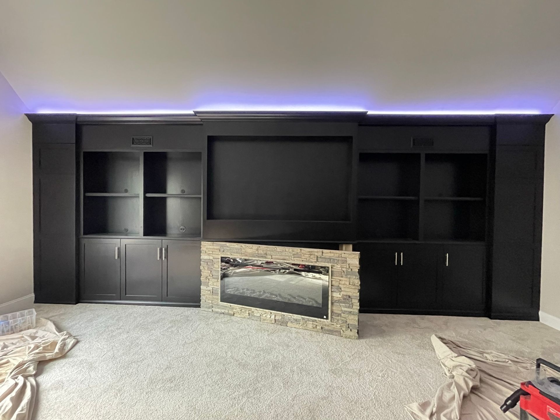 Black entertainment center with shelves, cabinets, fireplace, and TV. Purple LED lighting across the top.