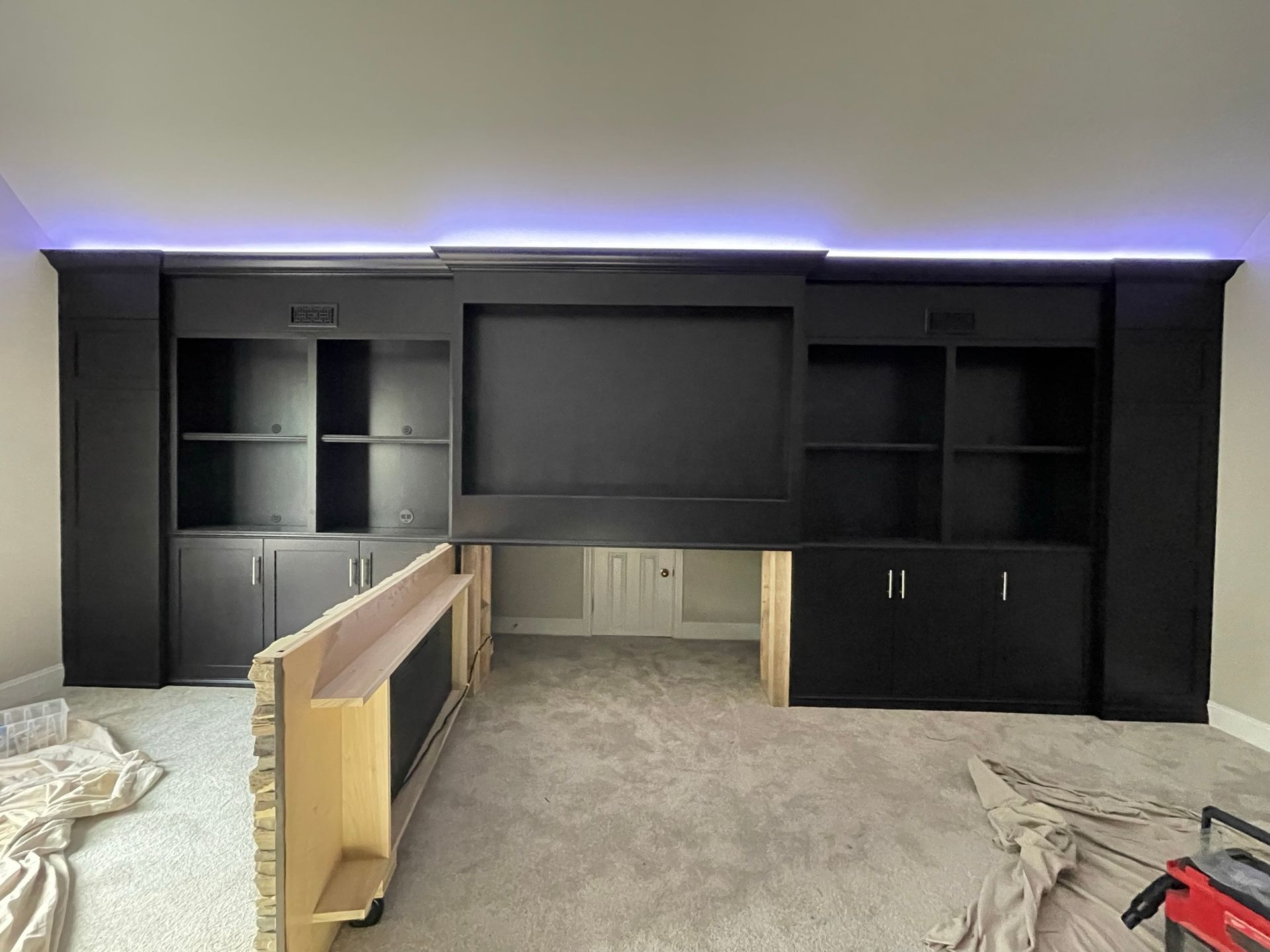 Black entertainment center with built-in shelves and a center space for a TV. Lit with blue light.