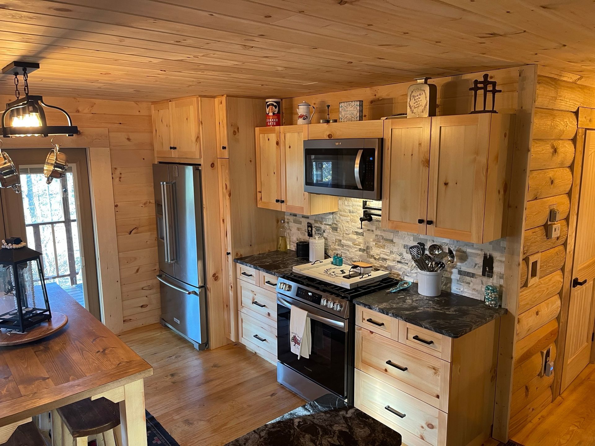Log cabin kitchen with wood cabinets, stainless steel appliances, and stone backsplash.